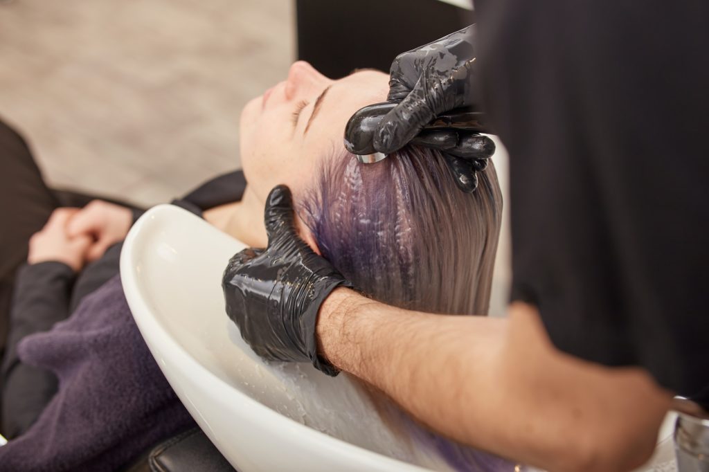 Hairdresser hands washing toning shampoo out of woman hair