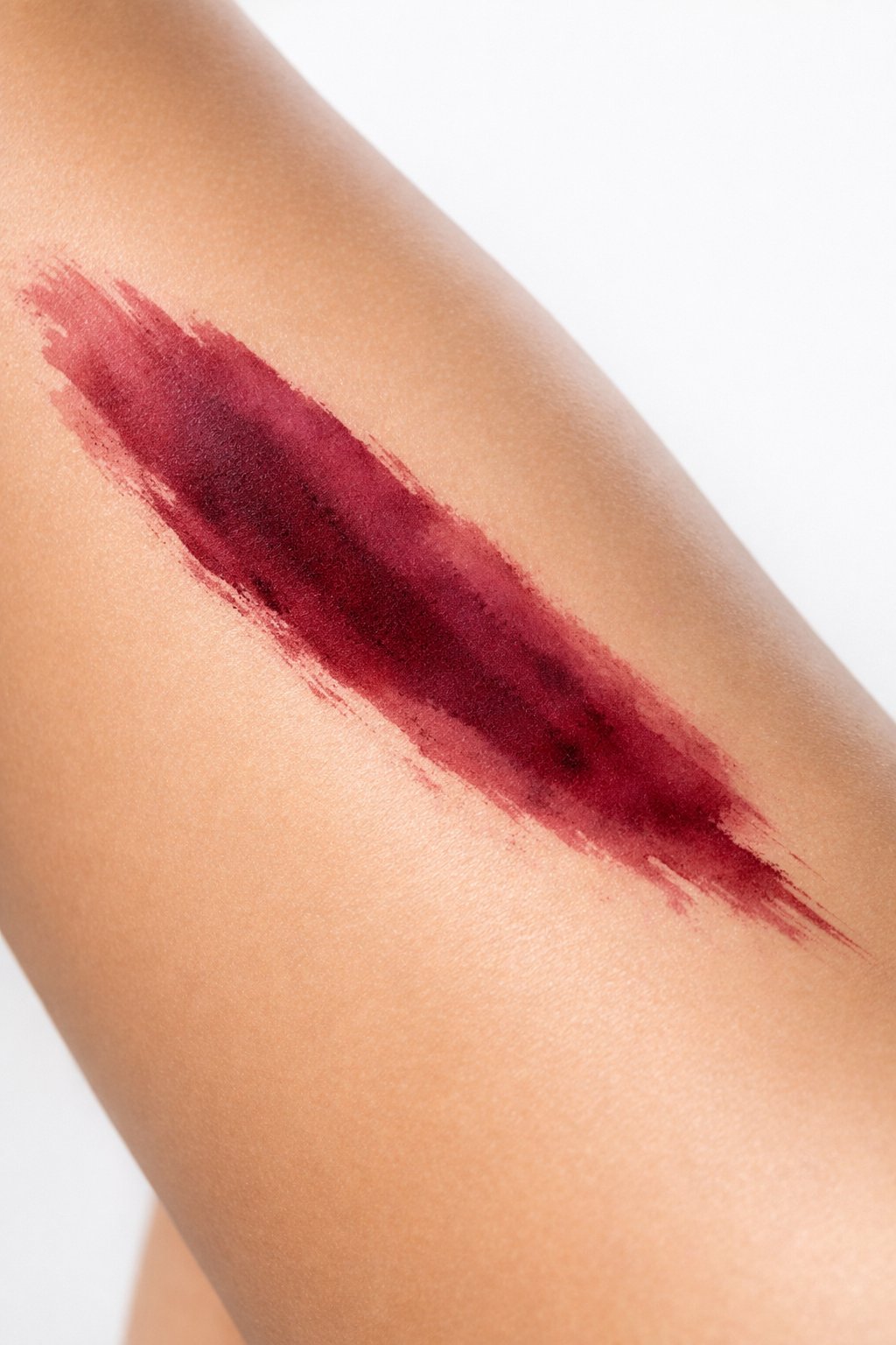 Diagonal view of the side thigh: a single, fluid brushstroke in a deep burgundy watercolor wash. The edges are feathered and soft, bleeding slightly into the skin.