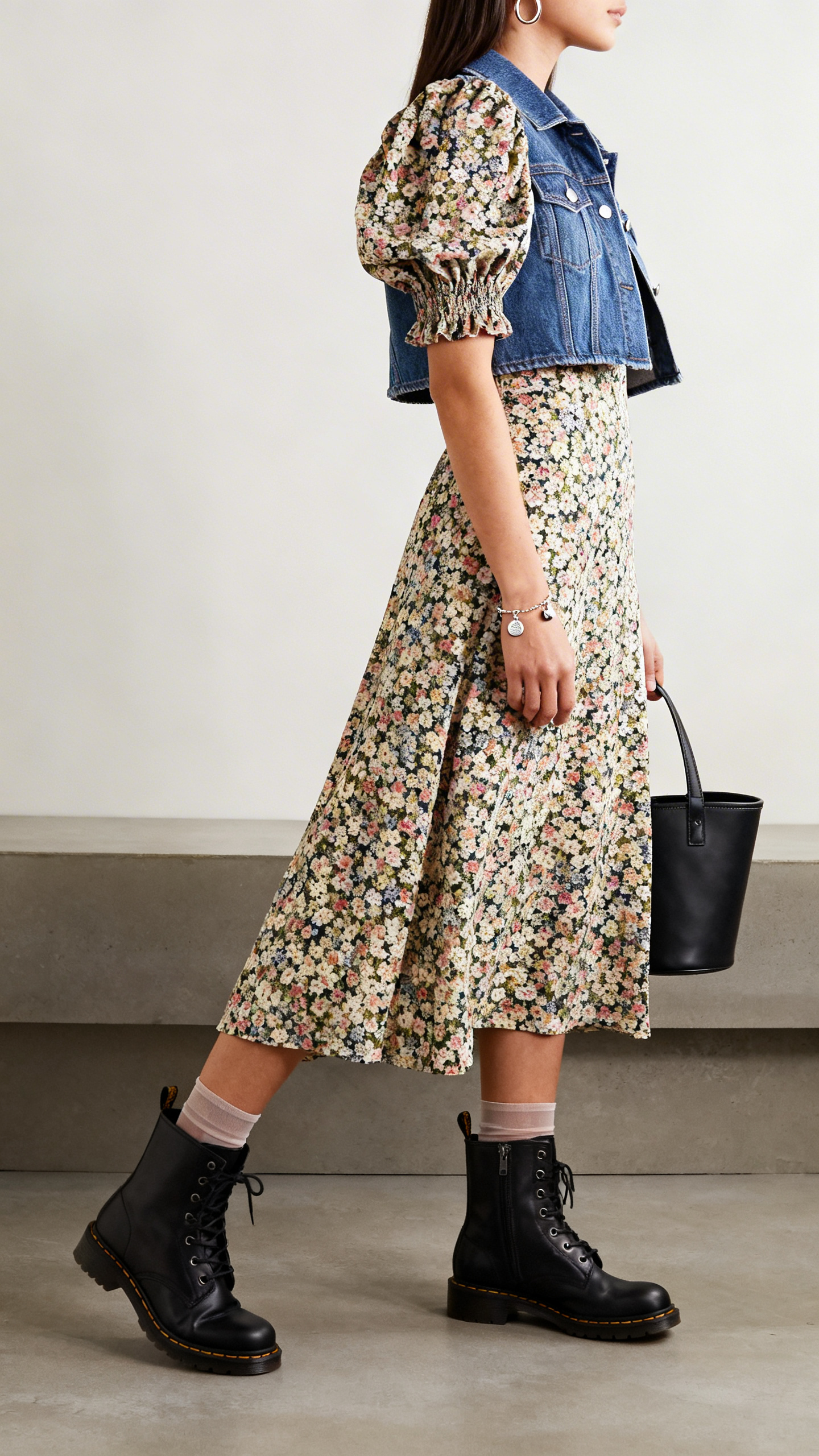 Bathroom mirror selfie: a woman in a floral midi dress with puff sleeves, black ankle moto boots, cropped denim jacket, bucket bag, simple hoops and a charm bracelet, sheer socks peeking above boots optional, side angle with face not visible, iPhone photo quality.