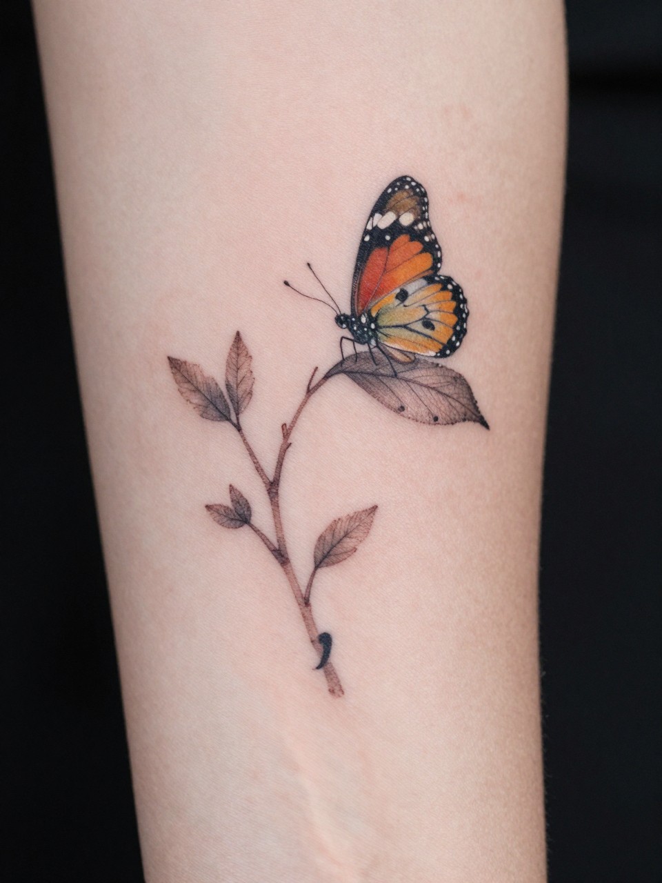 "Macro photograph of the inner arm tattoo: a delicate branch with a semicolon 'cocoon' and a settled butterfly on a leaf above it. A quiet, story-telling scene."