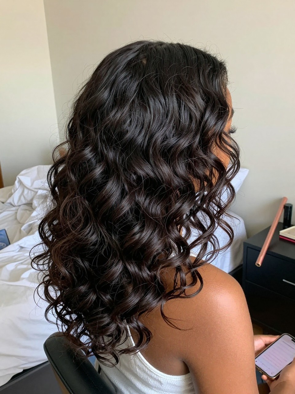 Photo of a black woman wearing overnight heatless waves, back-of-head view showing the pattern of waves, setting is a bedroom with morning light and rumpled sheets, containing the satin rod resting on her nightstand, iPhone photo quality.
