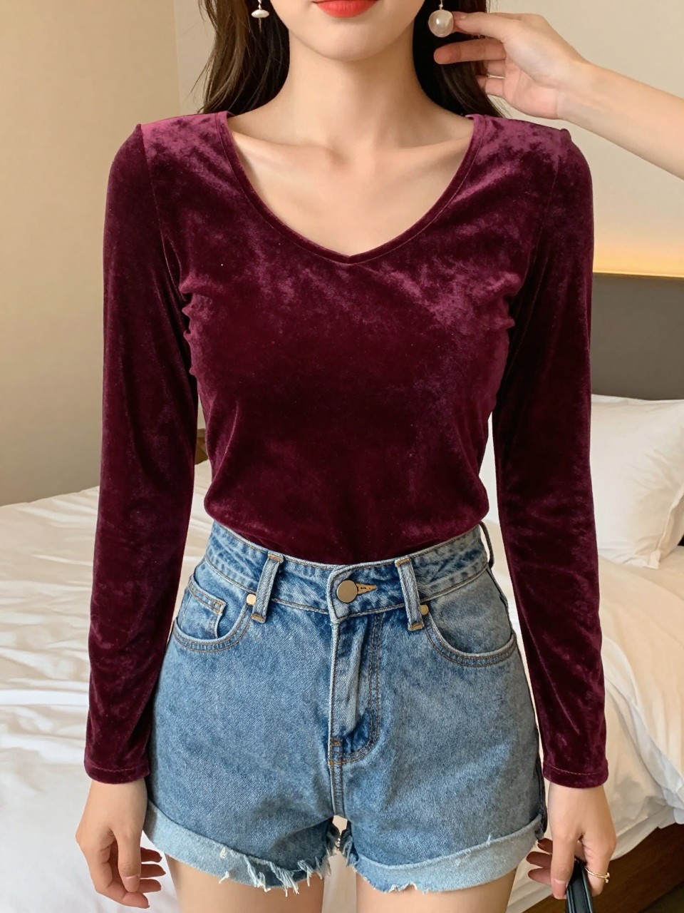 full picture of a woman in a velvet top and denim shorts, touching an earring, cropped at NECK so face doesn't show, in a feminine-themed bedroom, warm moody lighting, iPhone photo quality.