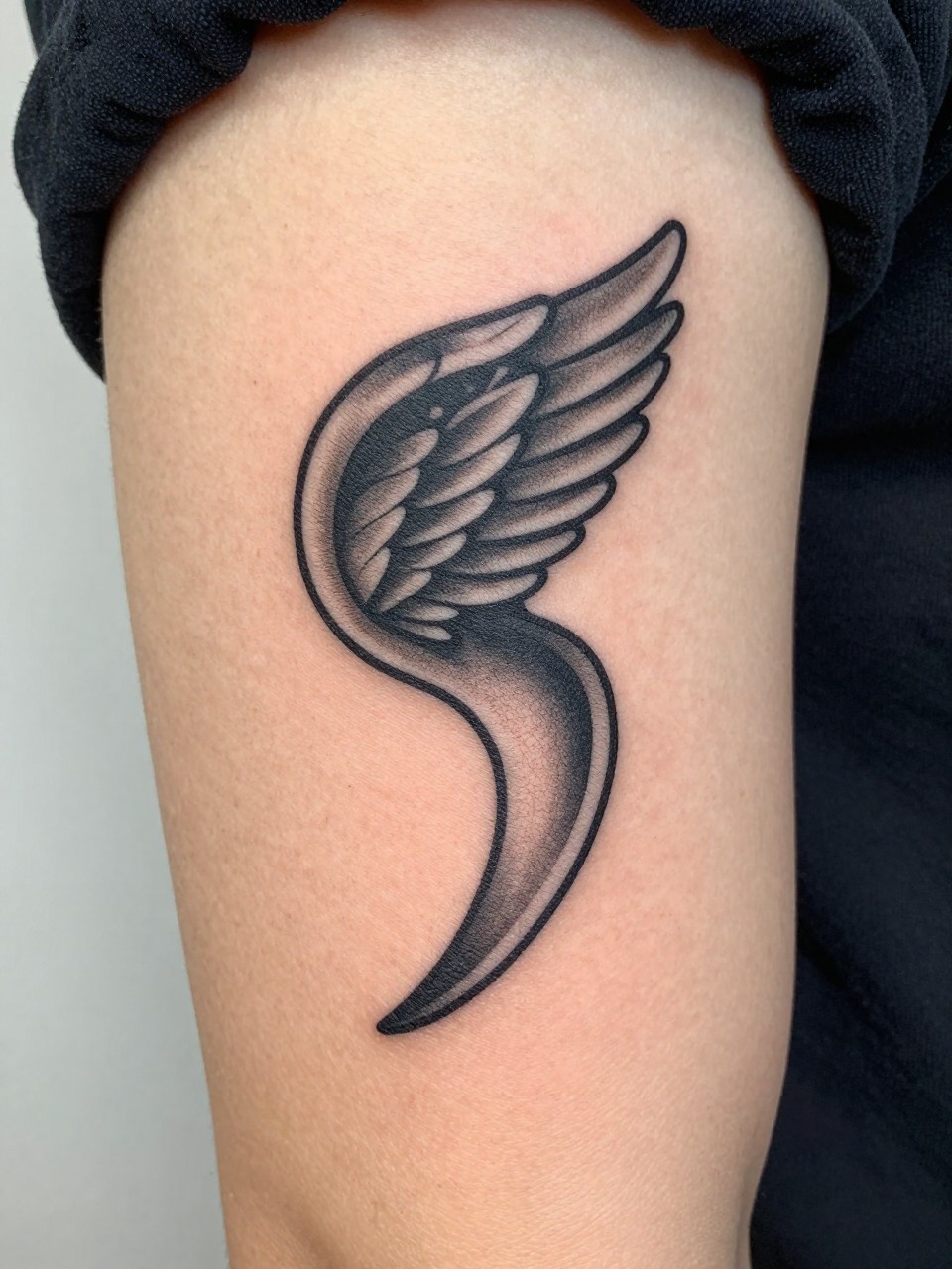  "Detailed view of the inner bicep tattoo: a bold, standalone semicolon where the interior of the comma shape holds a tiny, intricate wing pattern."