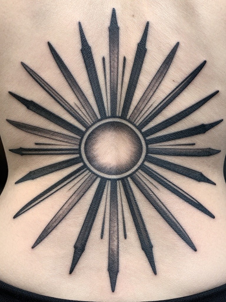 "Extreme close-up of the central radiating lines of an Art Deco sunburst tattoo. The pattern is perfectly symmetrical, with sharp, clean blackwork and subtle grey shading for depth, centered on the spine."