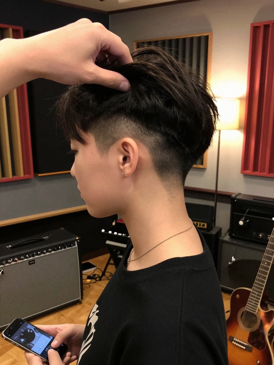 Photo of undercut choppy bob, hand pulling hair up to reveal undercut, in a music studio with instruments visible, warm lamp light creating cozy atmosphere, containing a guitar pick on the amplifier, iPhone photo quality.
