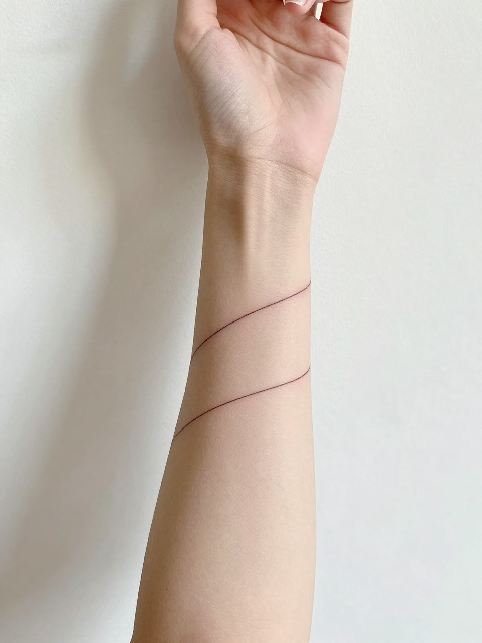 Image Prompt: "Close-up of a single-line spiral tattoo wrapping around a wrist and lower forearm. The arm is extended gracefully against a white wall with soft shadows. Bright, clean natural light. Minimalist and calm aesthetic."
