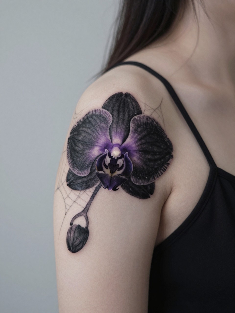 Close-up of a black orchid tattoo on the shoulder, with fine spiderweb details in the background. The orchid has intricate black and deep purple shading. She's wearing a thin-strapped black top. Soft, diffused light with a slight haze, mysterious and elegant aesthetic.