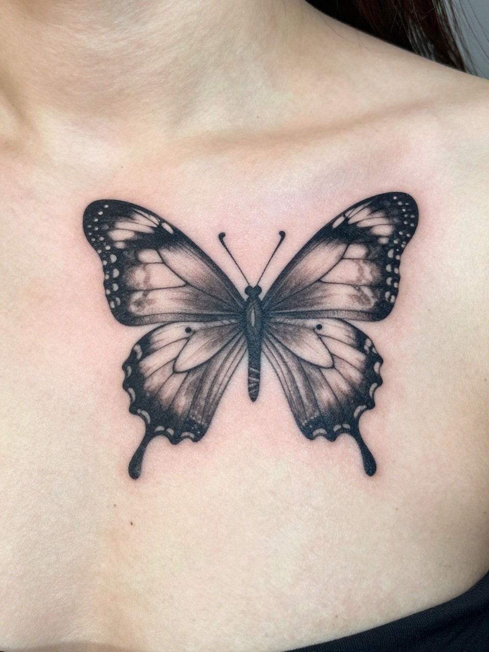 "Detailed view of the chest near the heart tattoo: one large, detailed butterfly wing curling around a small semicolon. A composition of protection and grace."