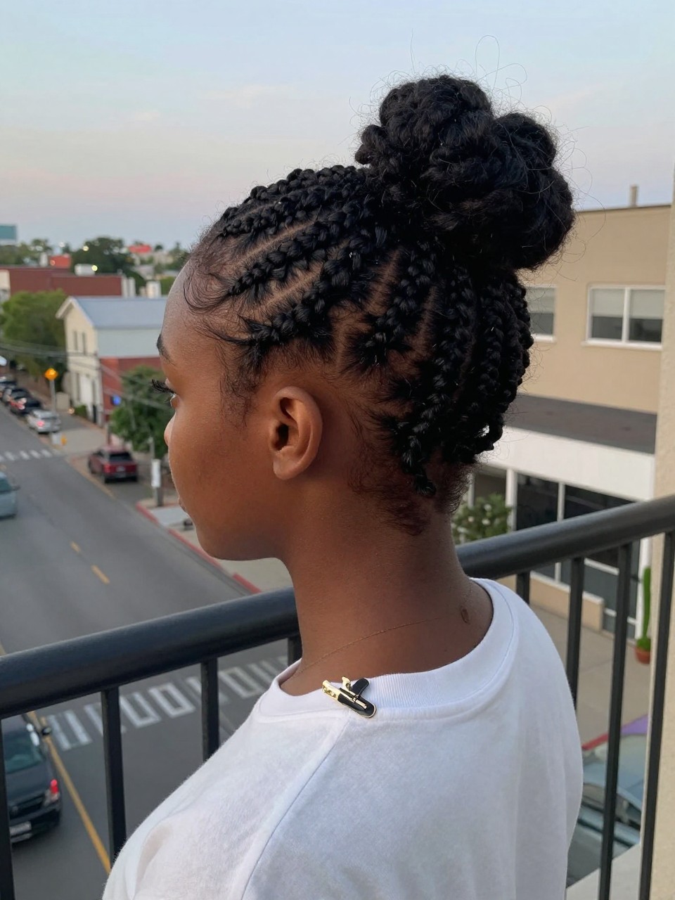 Photo of a teen black girl wearing a rope twist half-up, back-of-head view showing the twists meeting, setting: a balcony overlooking a city street at dusk, lighting: soft, fading natural light, containing a small hair clip clipped to her collar, iPhone photo quality.