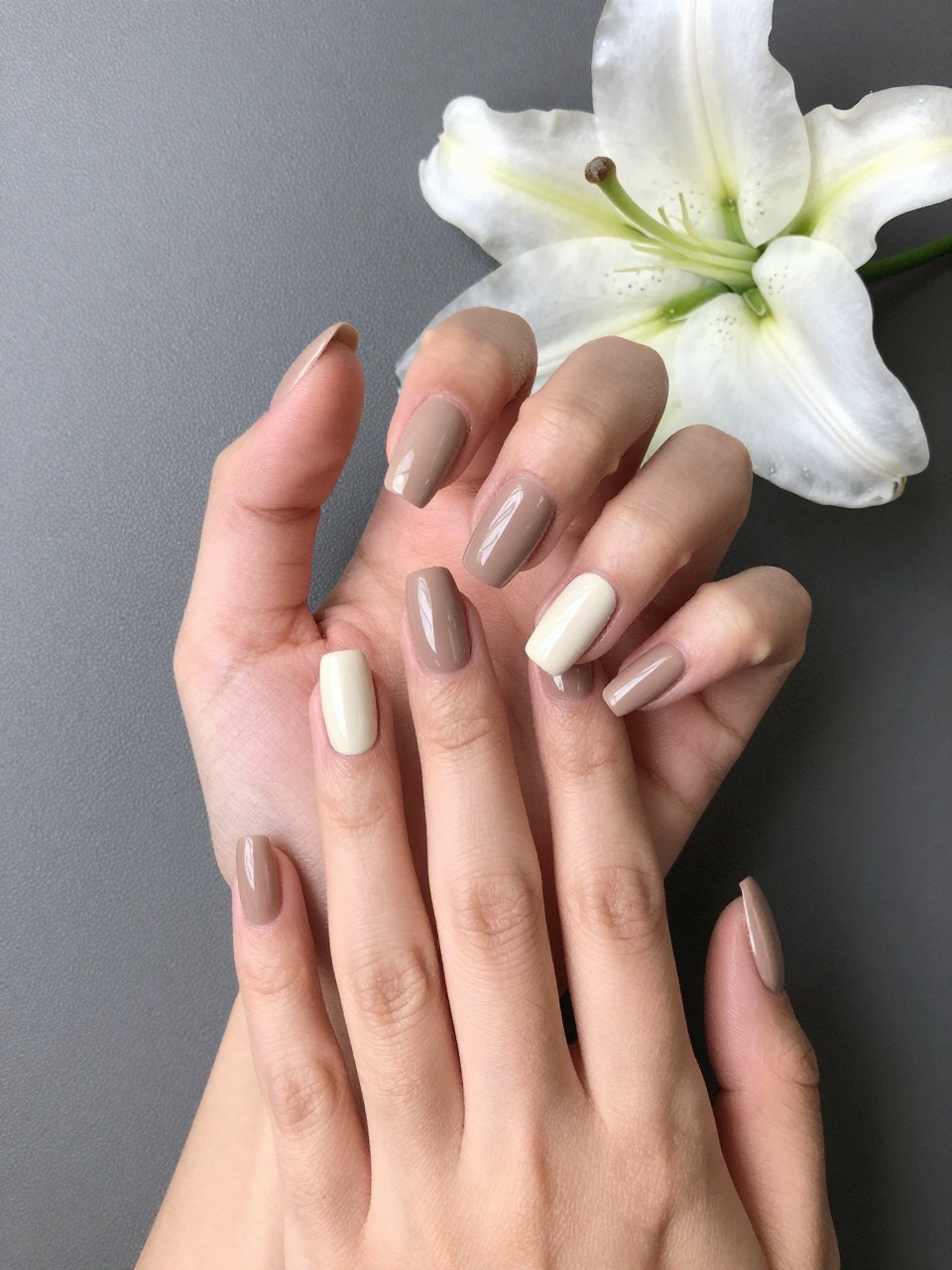 Bird's-eye view of one hand gently showcasing nail set. The nails color is  a creamy hazelnut brown. Each ring finger features a single, graceful white lily with a green stem. The look is pure and sophisticated.