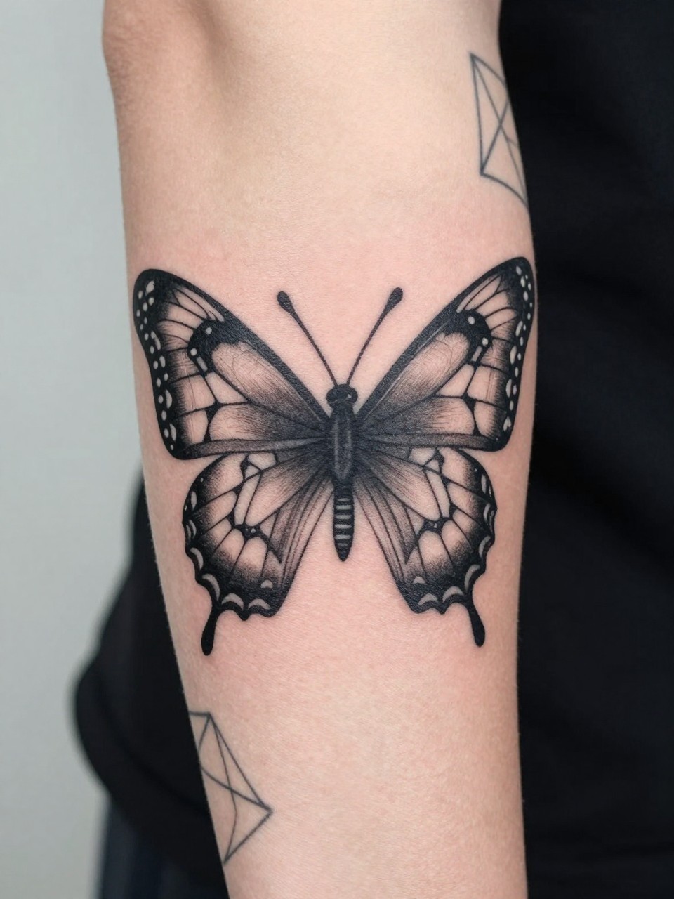  "Detailed shot of a forearm tattoo: a butterfly with geometric, lace-like patterns within its wings, seamlessly connected to other geometric shapes on the arm. Crisp, precise lines and shading."