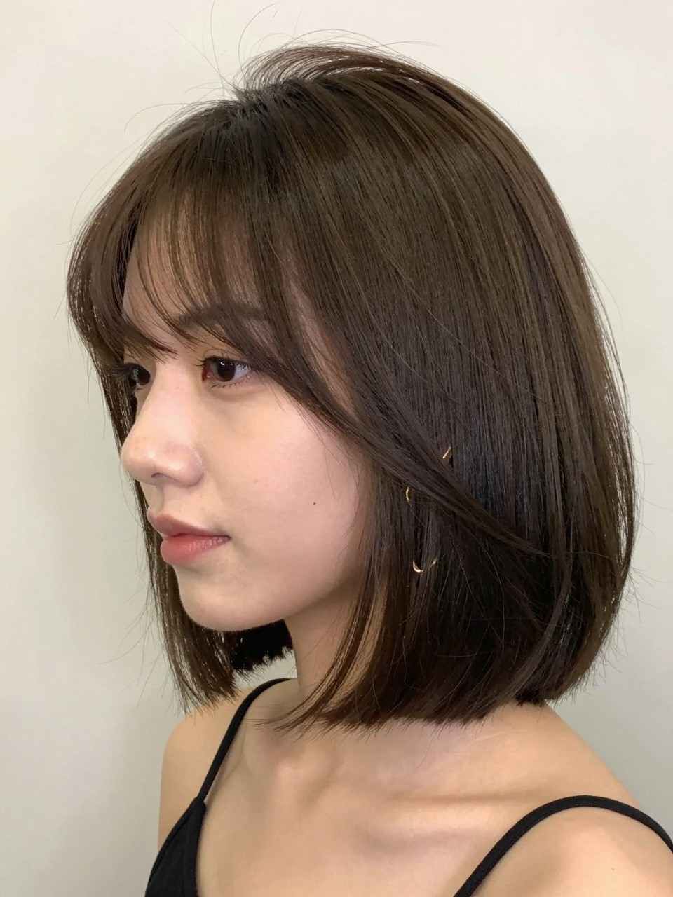 Photo of a woman wearing a jaw-length side-part bob with soft crown lift and lightly tucked ends, with the haircut fully visible and clearly defined, shot from a three-quarter angle, in a soft neutral studio, with soft indoor lighting, showing the haircut shape, layers, ends, bangs, and texture clearly, including simple gold earrings, latest iPhone photo quality.
