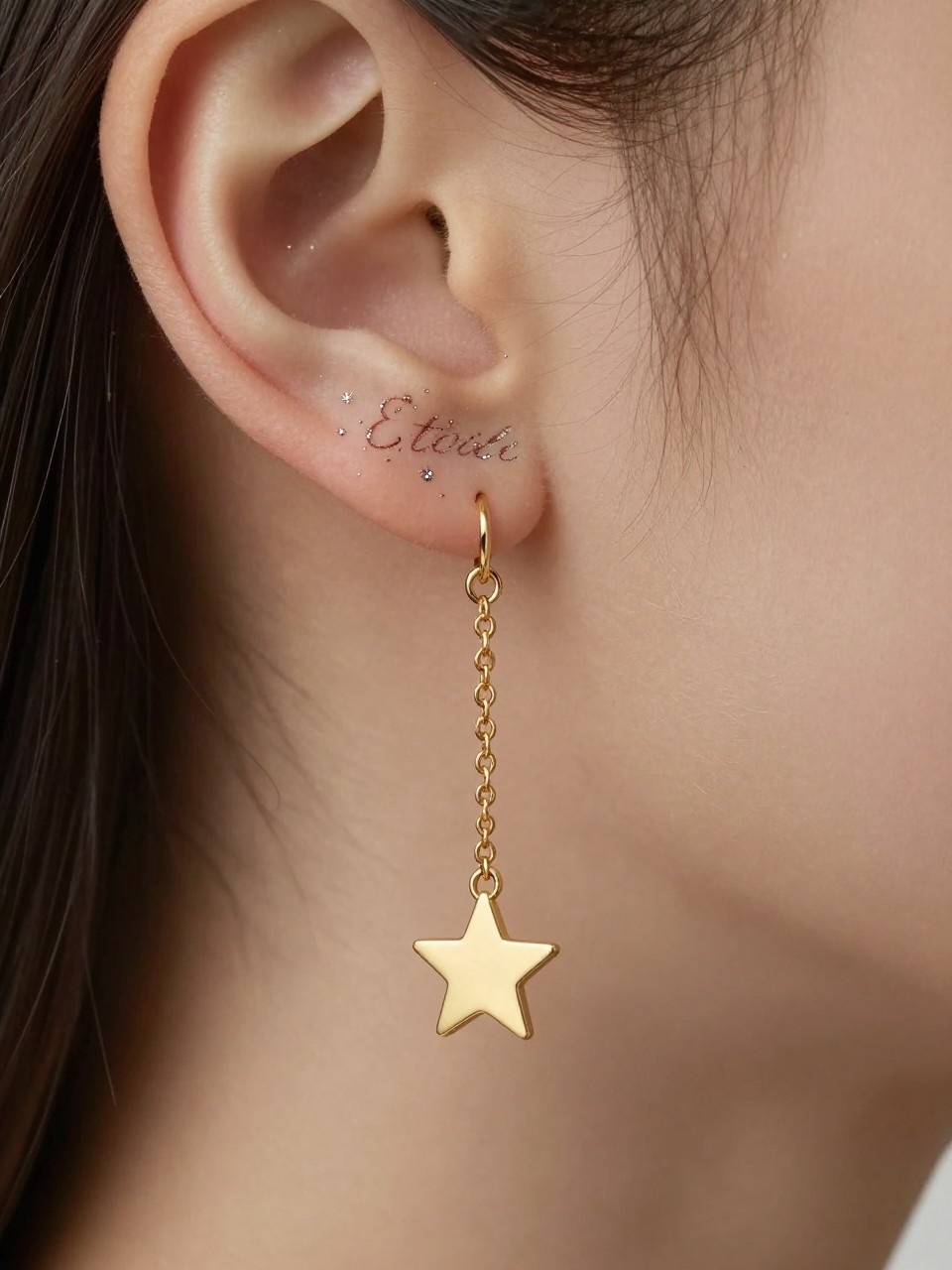"Macro shot of 'Étoile' in a delicate, star-dotted script behind the ear. A single, tiny gold star charm on a chain lies against the neck. Celestial and subtle."