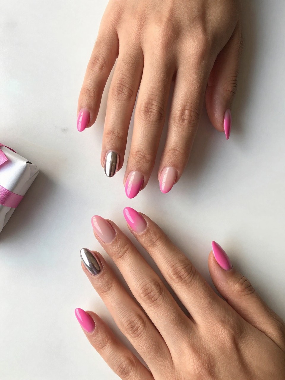 90-degree overhead top-down view of two feminine black hands with almond medium nails.
The manicure features a full hot pink base on most nails with one mirror chrome accent nail on each hand.
Include reflective glossy gel finish.

Hands are posed fingers gently spread.

Scene set on a white marble surface with a small wrapped gift nearby.

Bright natural daylight with soft shadows, hyper-realistic lifestyle photography, sharp focus on nails, natural skin texture, realistic hands, no extra fingers.