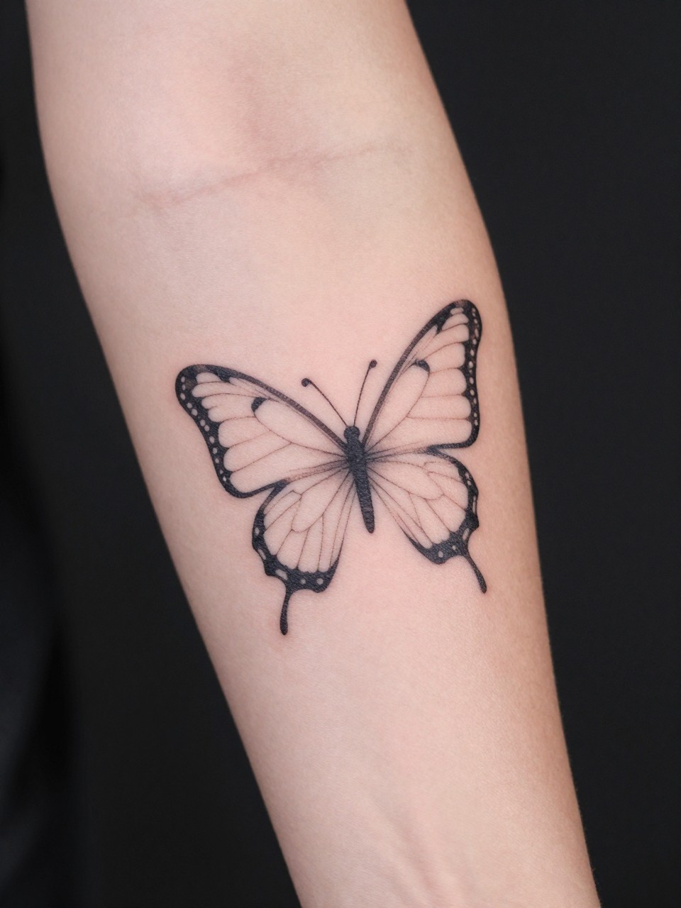 "Close-up of an upper arm, showing a single, perfect line that loops to create a butterfly shape on the bicep. The arm is against a plain, dark background. Focus on the ingenuity of the continuous line."