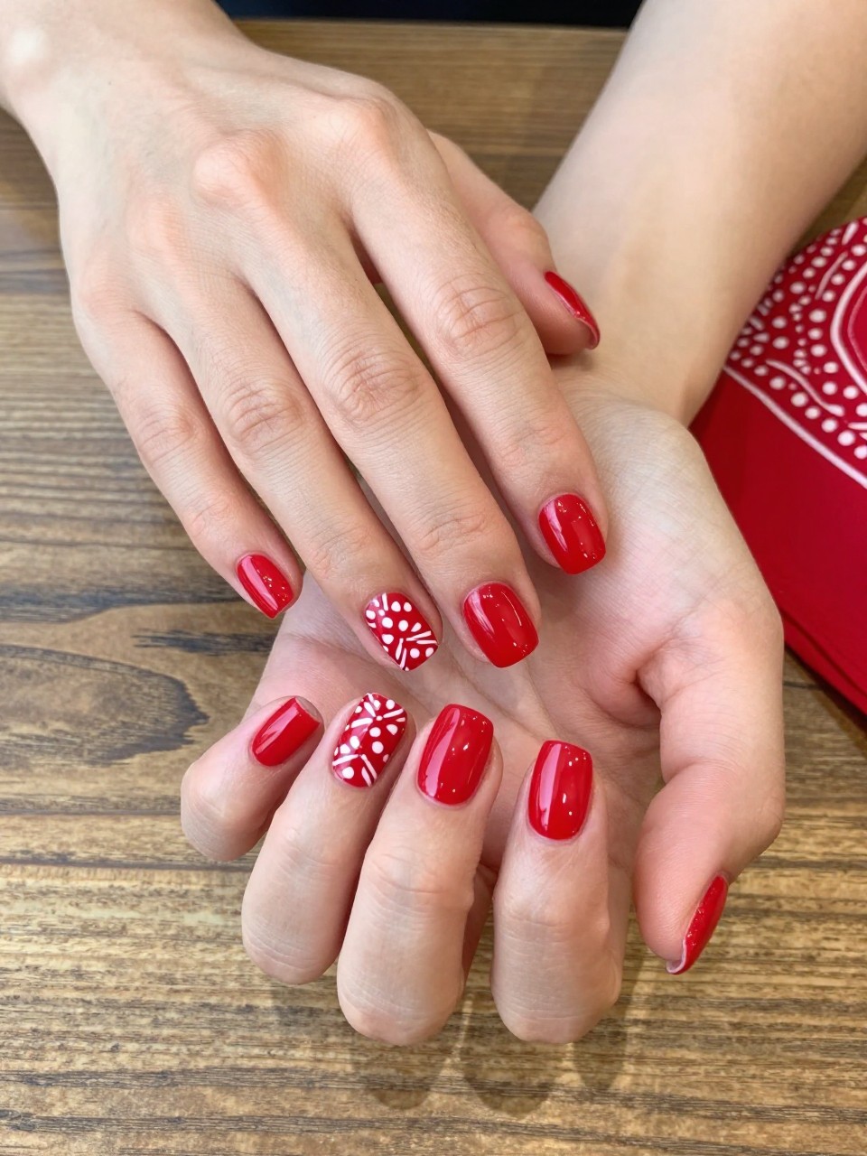 90-degree overhead top-down view of two feminine hands with square short nails.
The manicure features a bright red base with white bandana inspired western patterns across the nails.
Include glossy gel finish.

Hands are posed fingers gently spread.

Scene set on a wooden table with a red bandana cloth nearby.

Bright natural daylight with soft shadows, hyper-realistic lifestyle photography, sharp focus on nails, natural skin texture, realistic hands, no extra fingers.