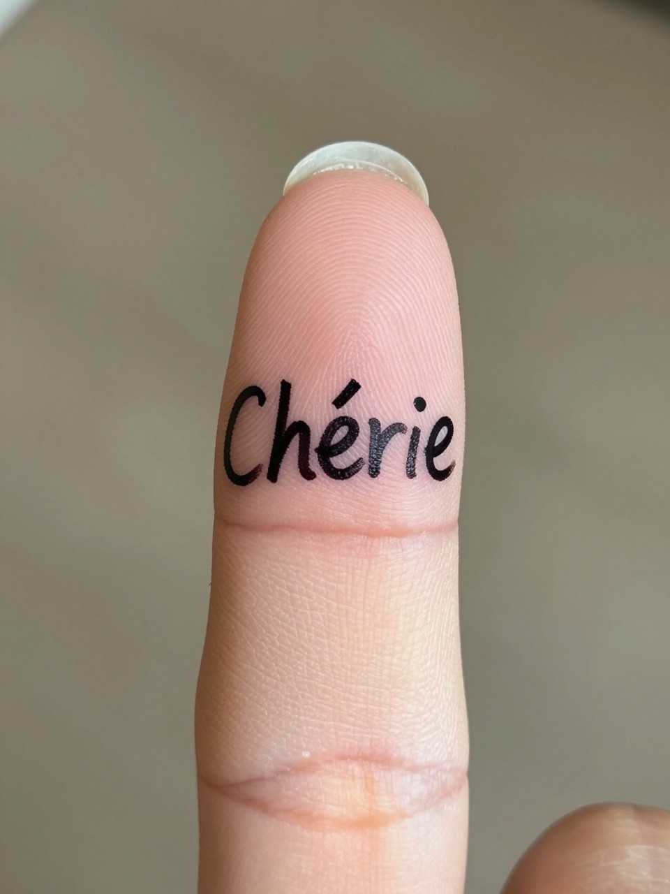  "Extreme close-up of 'Chérie' in a playful, handwritten script on the finger. Personal and sweet focus."