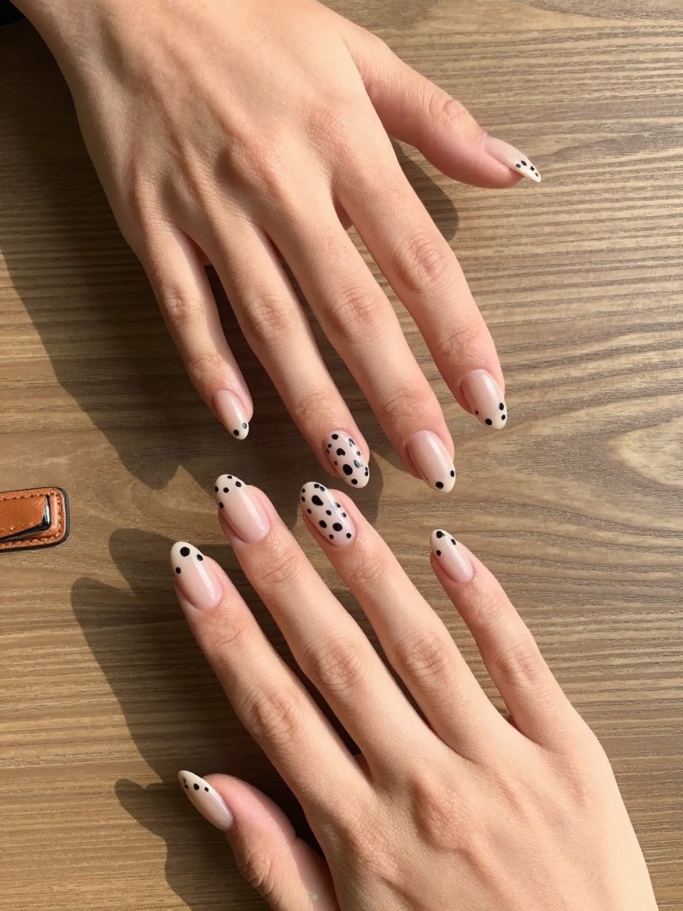 90-degree overhead top-down view of two feminine black hands with almond medium nails.
The manicure features a soft nude base with black cow print spots across each nail.
Include glossy gel finish.

Hands are posed fingers gently spread.

Scene set on a wooden table with a small leather belt nearby.

Bright natural daylight with soft shadows, hyper-realistic lifestyle photography, sharp focus on nails, natural skin texture, realistic hands, no extra fingers.