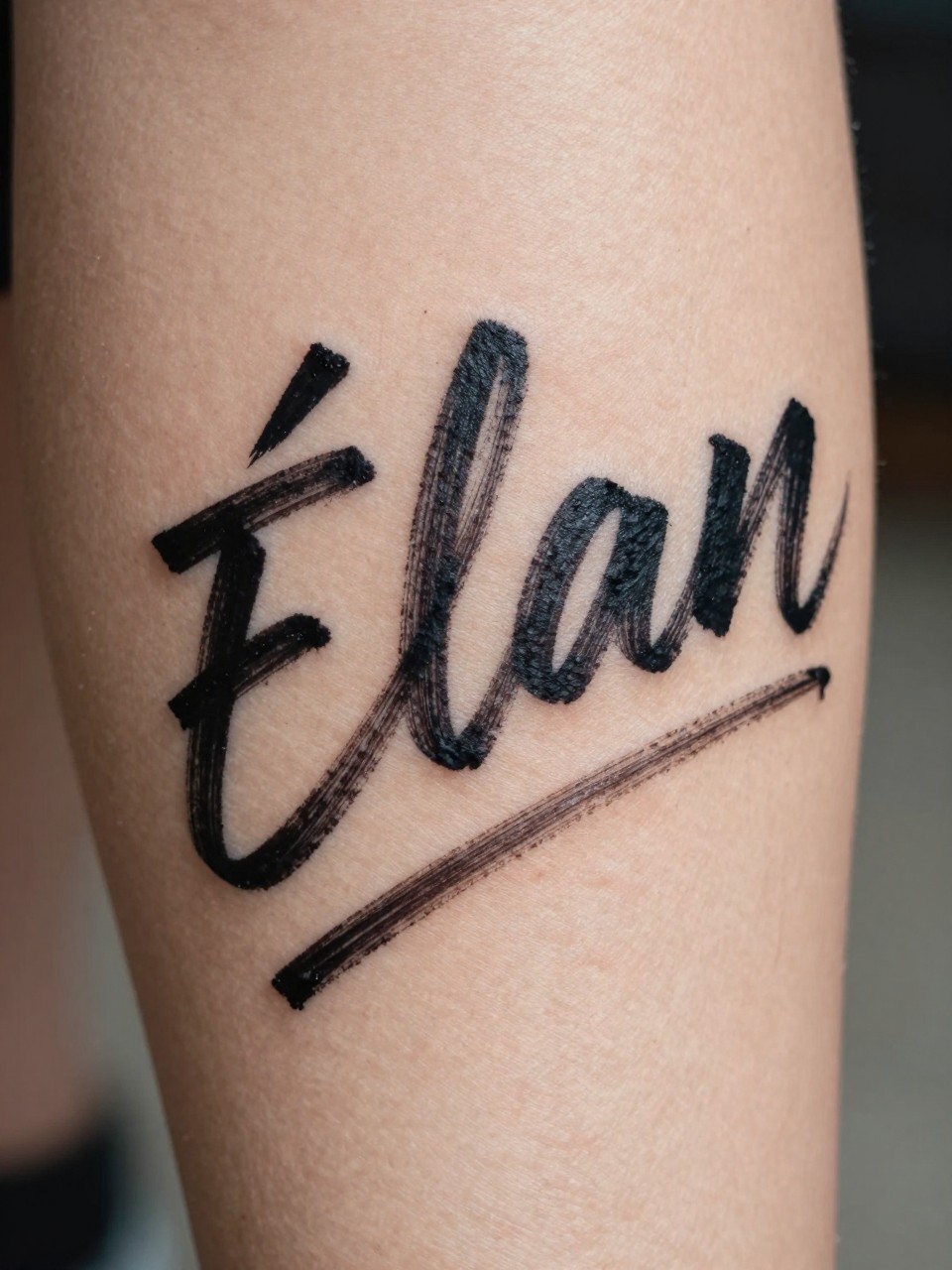"Macro shot of 'Élan' in dynamic, brushstroke-style script on the calf, as if written quickly. Energetic and artistic focus, suggesting movement."