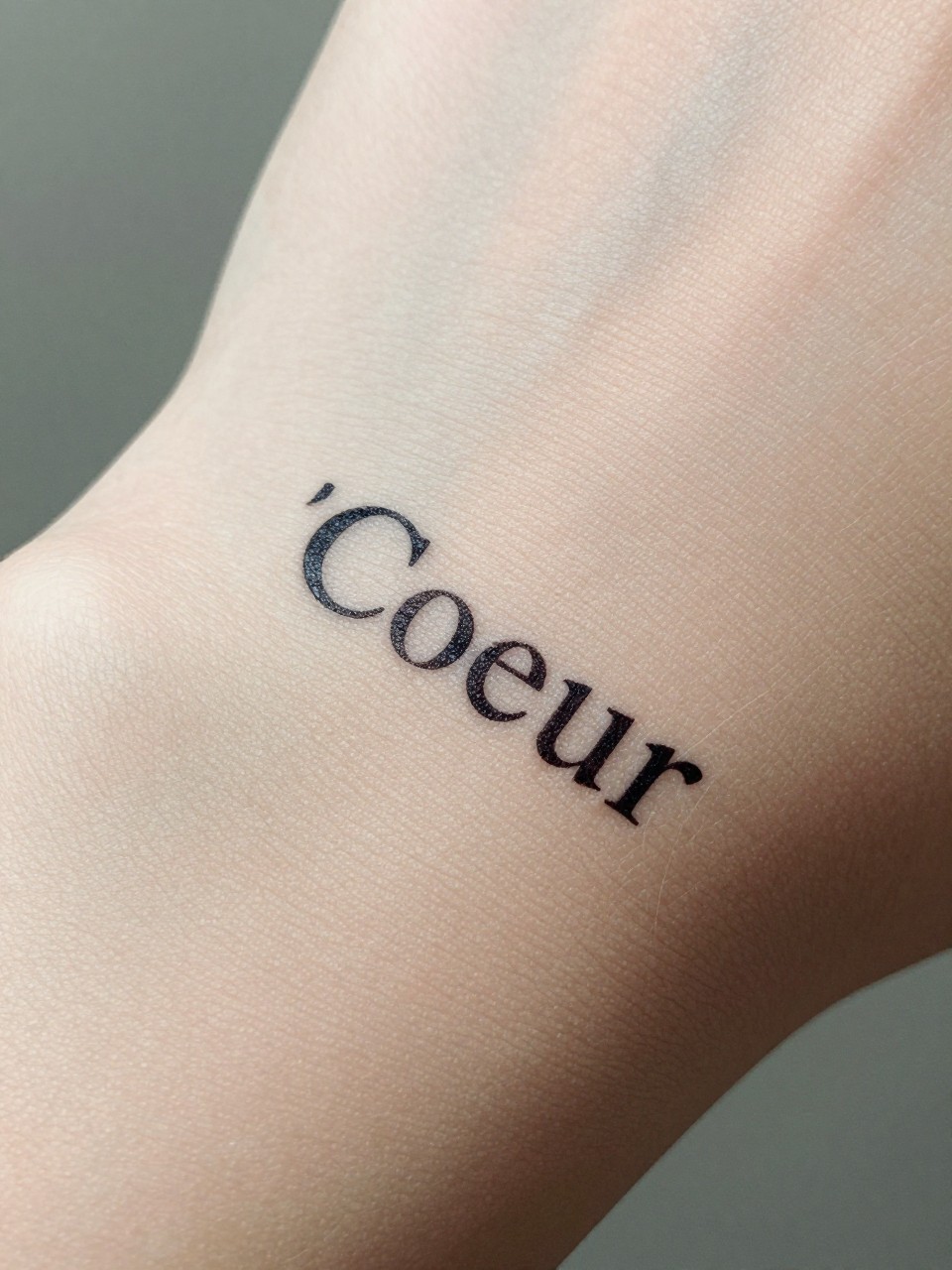 "Macro photograph of 'Coeur' in a classic, elegant font on the wrist, directly over the pulse point. The skin is bare, making the connection to the heartbeat obvious."