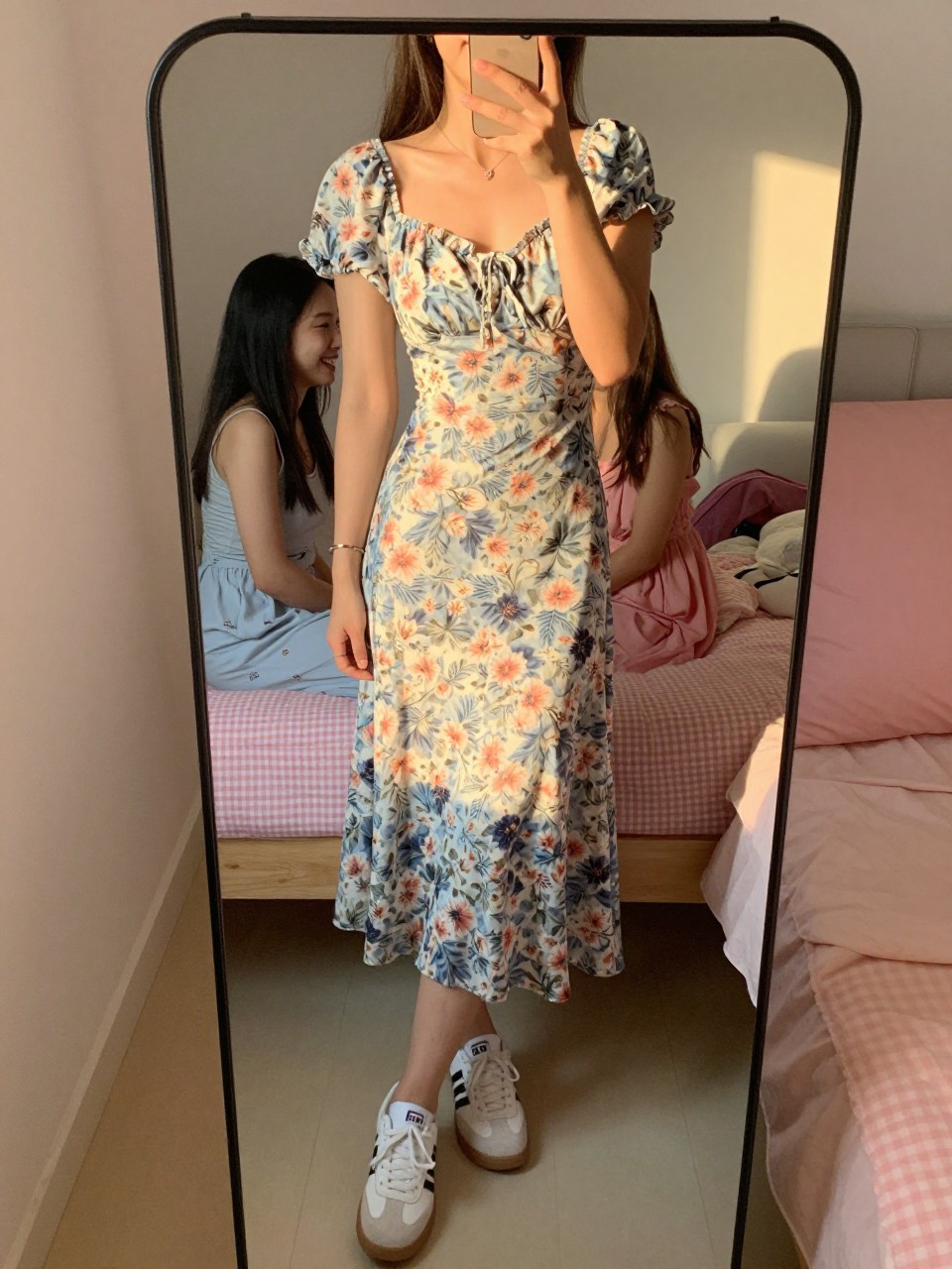 iPhone mirror selfie of a woman in a floral midi dress and white sneakers, laughing with friends, cropped at the neck so face doesn't show, in a feminine-themed bedroom, evening golden hour lighting, iPhone photo quality.
