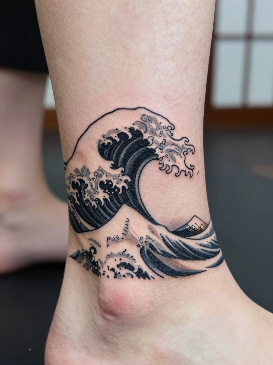 design-focused close-up of a clean Japanese wave tattoo on the ankle, small curling wave, black and grey ink, crisp linework, soft shading, minimalist traditional style, realistic skin texture, minimal blurred background, modern tattoo inspiration photo (no watermarks on images)