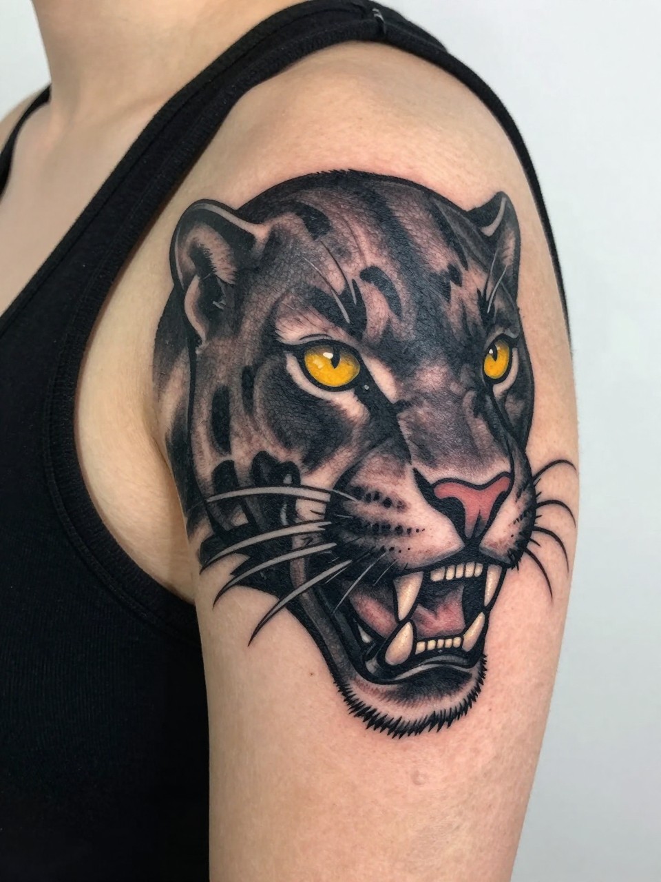 Image Prompt: "Extreme close-up of a bold black panther head tattoo on the shoulder. Heavy black shading, yellow eyes suggested by negative space. She's wearing a simple black tank top. Bright natural light shows every detail of the bold lines."