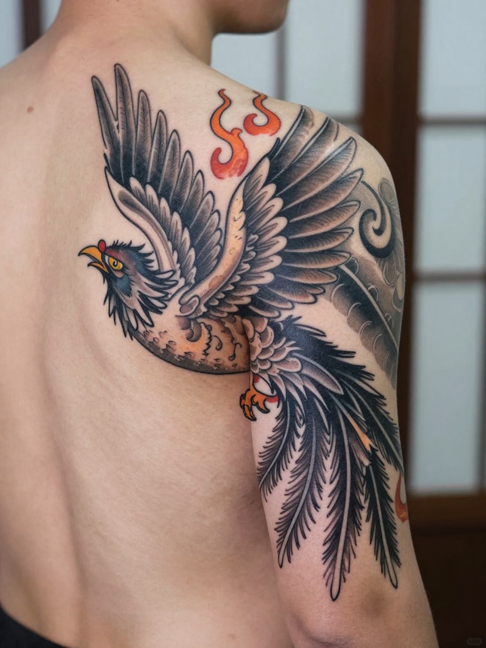 design-focused close-up of a traditional Japanese phoenix tattoo on the back or upper arm, wide wings, long feather details, flame accents, black and grey ink, strong traditional linework, realistic skin texture, minimal blurred background, modern tattoo inspiration photo (no watermarks on images)