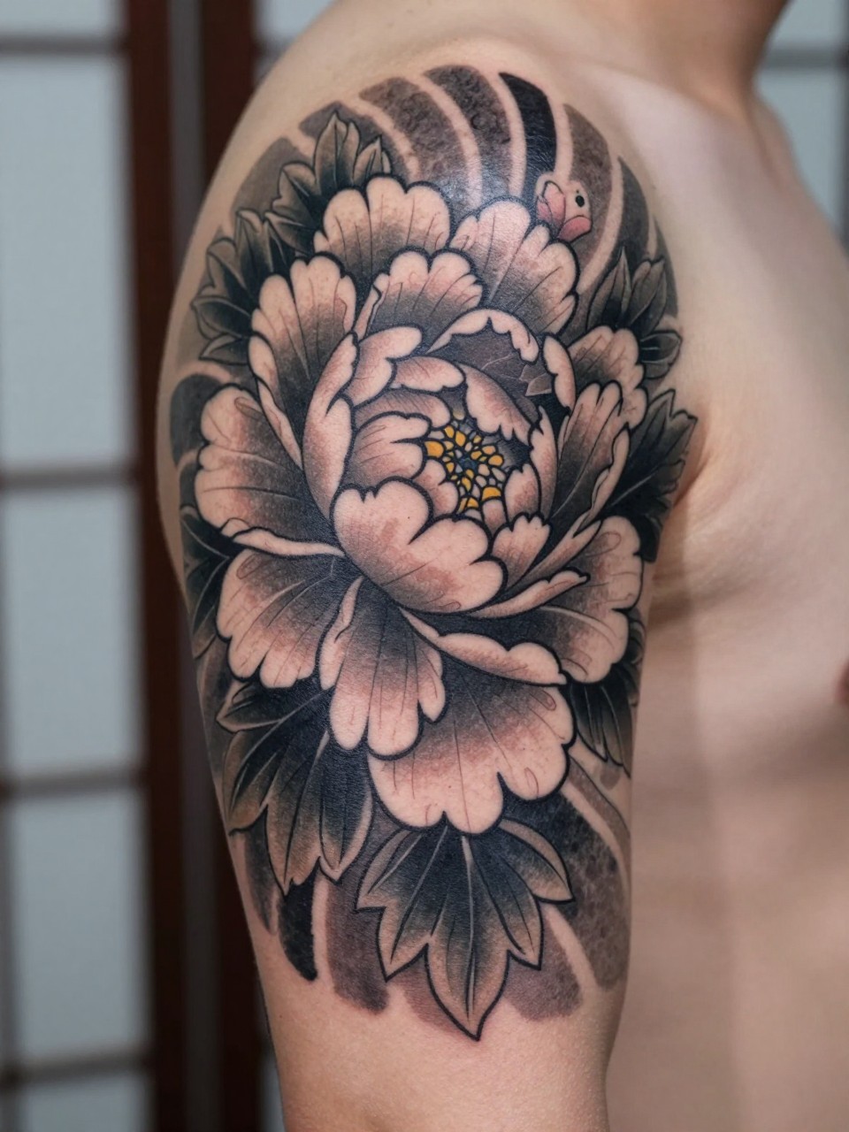 close-up of a Japanese peony armband tattoo on a man's upper arm, blooming peony flowers wrapping around the arm, black and grey ink, layered petals, bold traditional linework, soft shading, realistic skin texture, design-focused close-up, blurred neutral background, modern tattoo photography (no watermarks on images)