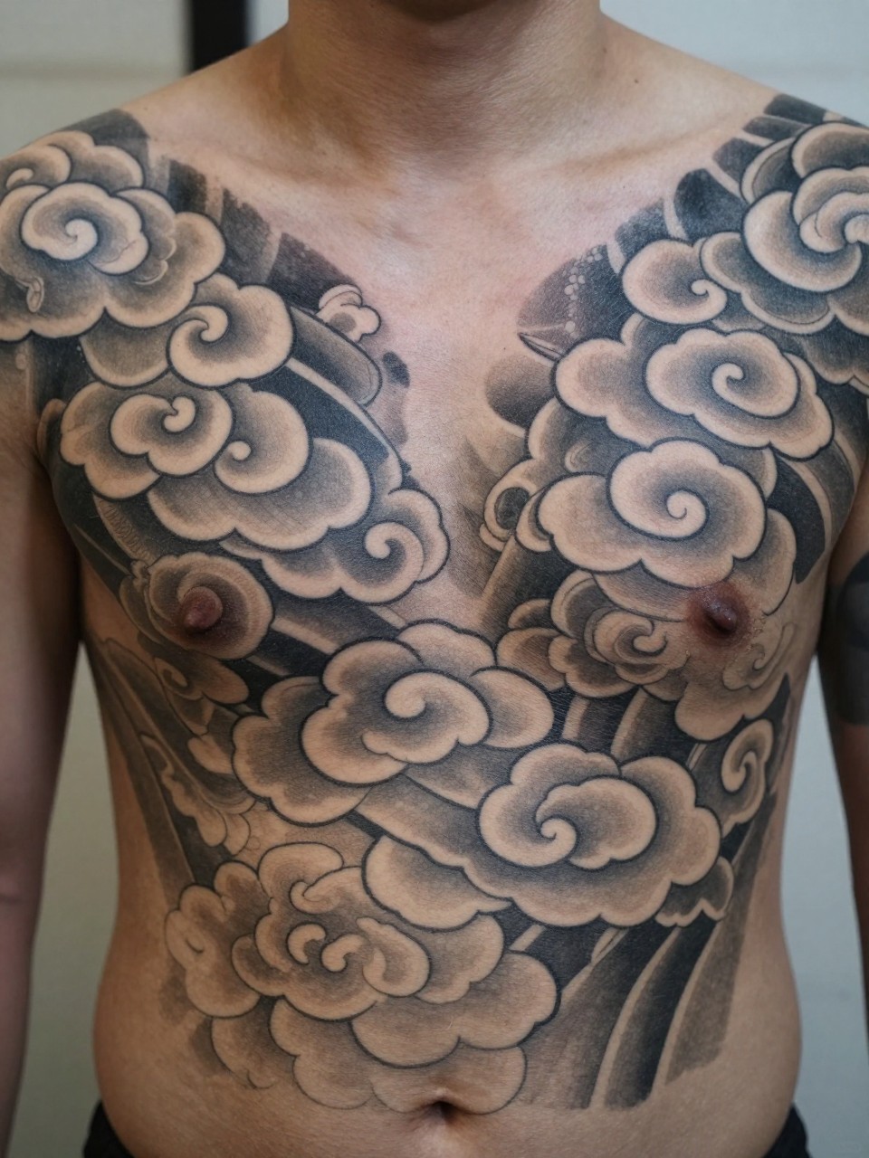 extreme close-up of a full chest Japanese cloud tattoo, layered traditional cloud forms spreading across the chest, black and grey ink, bold linework, smooth shading, realistic skin texture, soft minimal background, design-focused tattoo inspiration photography (no watermarks on images)