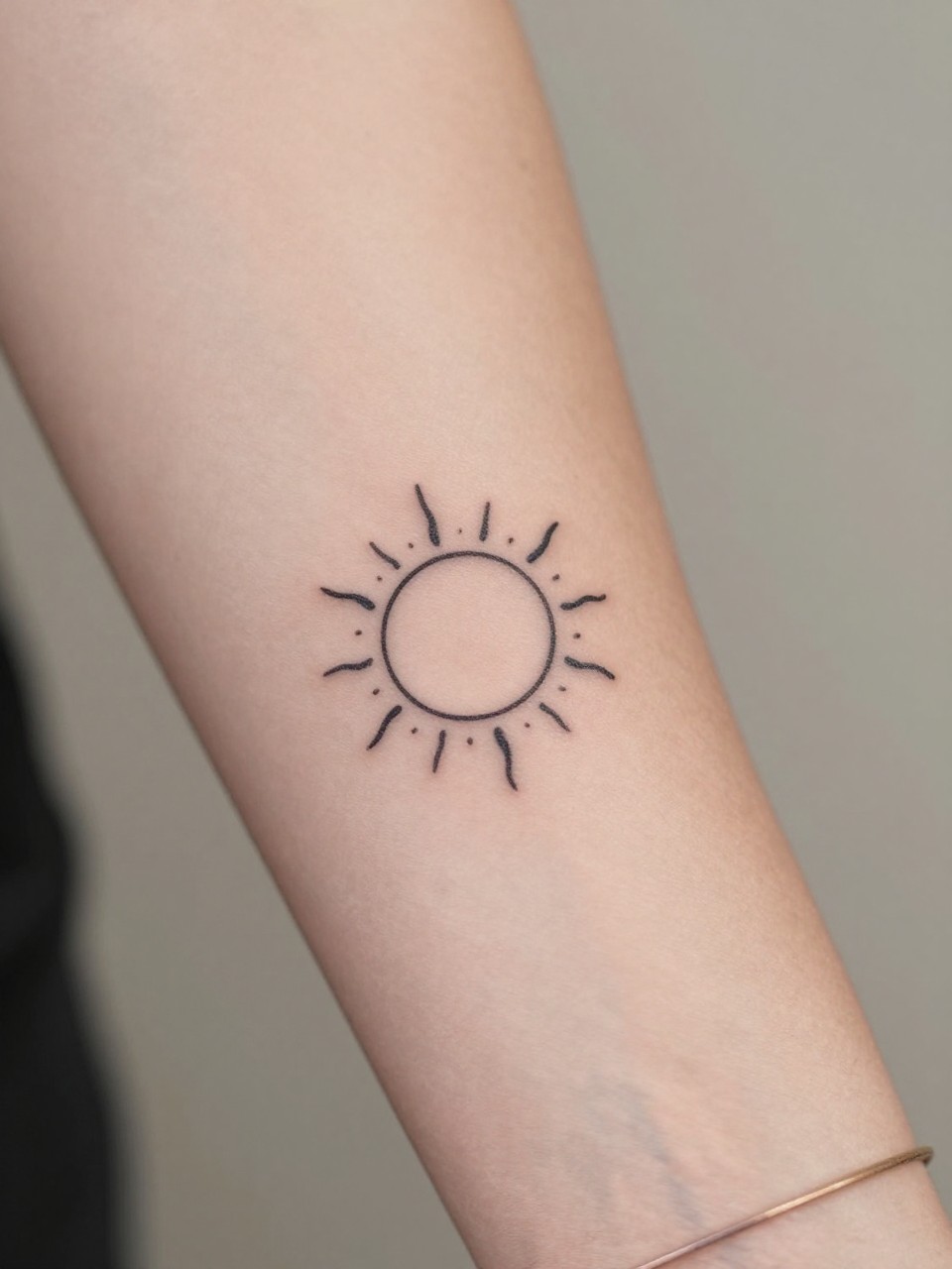 macro shot of a tiny sun tattoo on women's wrist, clean black ink, small circle with thin simple rays, minimalist earthy boho hippie design, realistic skin texture, bracelet nearby, tight crop, design-first tattoo composition, soft neutral background, tattoo inspiration image (no watermarks on images)