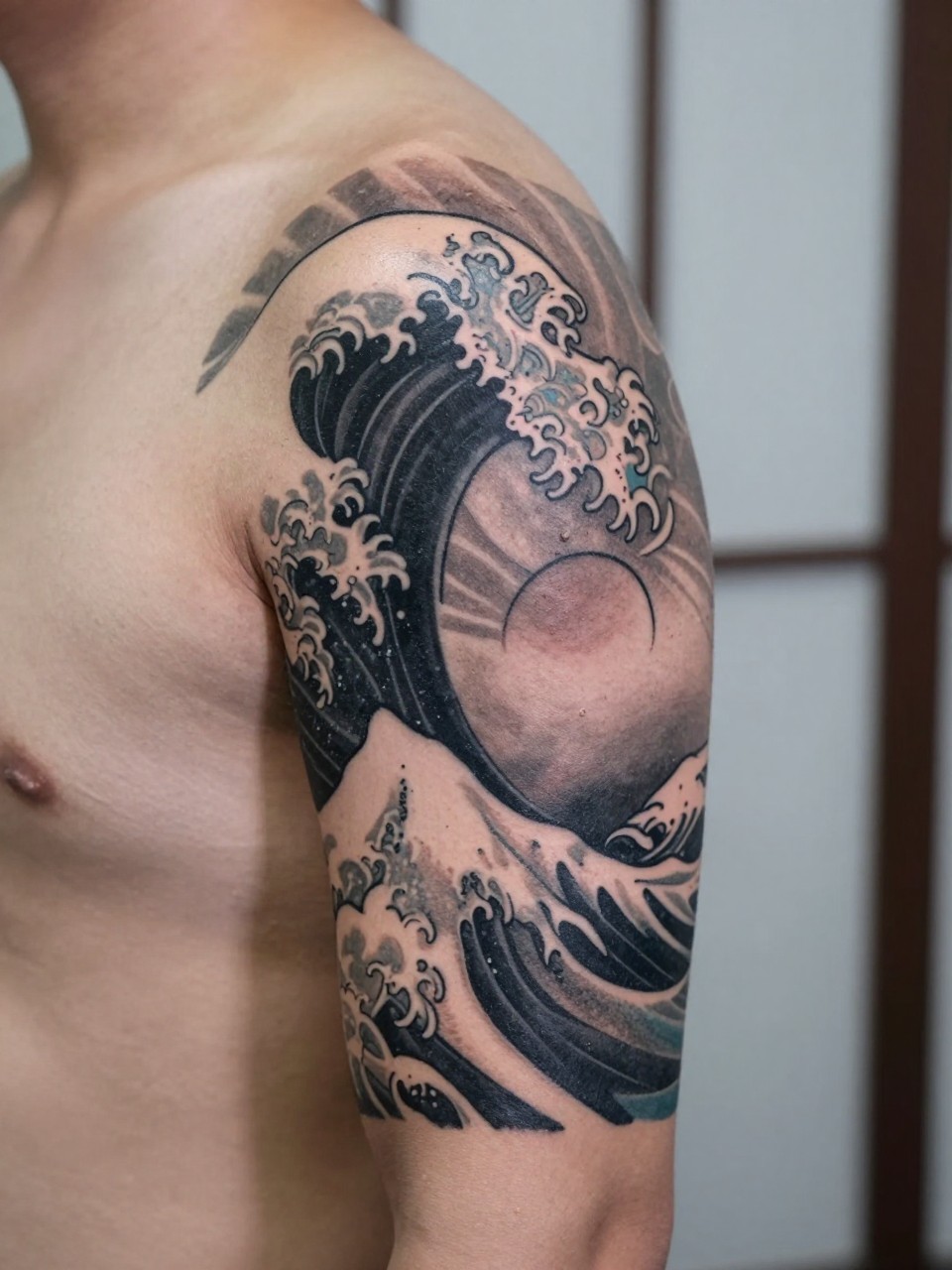 design-focused close-up of a Japanese wave and rising sun armband tattoo on a man's upper arm, bold wave forms wrapping around the arm with simple sun detail, black and grey ink, traditional linework, soft shading, realistic skin texture, minimal blurred background, modern tattoo inspiration photo (no watermarks on images)