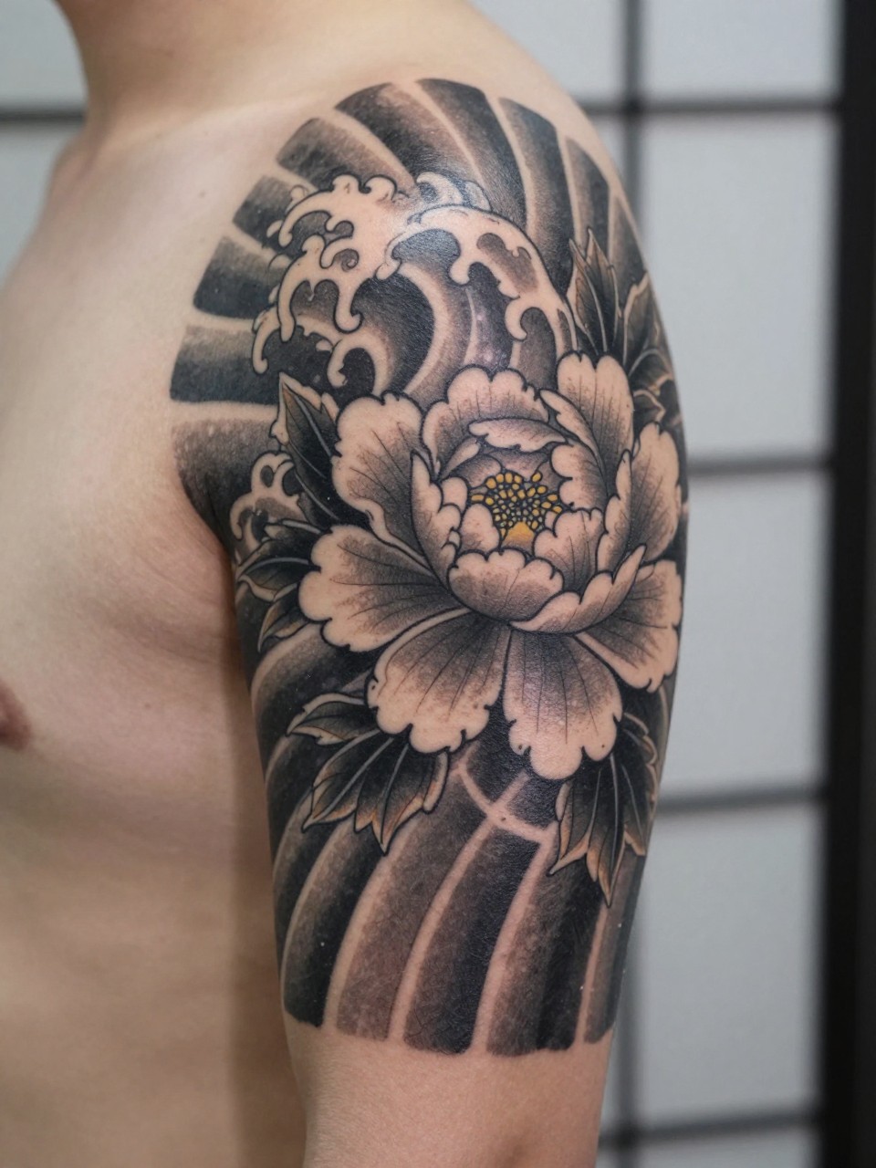 close-up of a clean Japanese wave tattoo with peony accent on the upper arm, bold wave form with one peony flower, black and grey ink, crisp traditional linework, soft shading, realistic skin texture, design-focused close-up, blurred neutral background, modern tattoo photography (no watermarks on images)