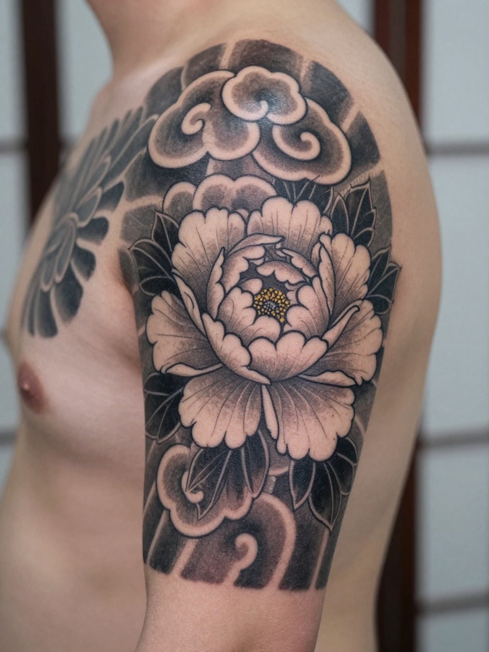 design-focused close-up of a Japanese cloud and peony sleeve starter tattoo on the upper arm, one peony bloom with bold cloud detail around it, black and grey ink, traditional linework, soft shading, realistic skin texture, minimal blurred background, modern tattoo inspiration photo (no watermarks on images)