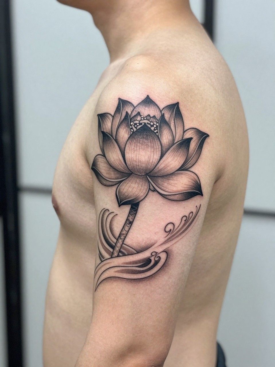 design-focused close-up of a Japanese lotus and water armband tattoo on a man's upper arm, lotus bloom with flowing water detail wrapping around the arm, black and grey ink, clean traditional linework, soft shading, realistic skin texture, minimal blurred background, modern tattoo inspiration photo (no watermarks on images)