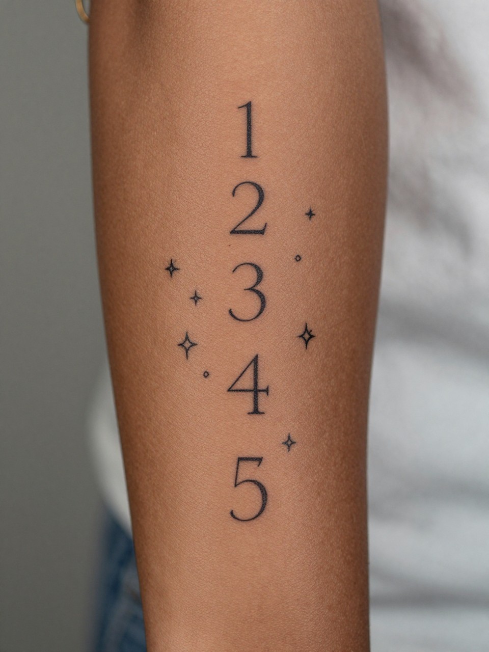 extreme close-up of an angel number and sparkle sleeve tattoo on deep brown skin, fine line numbers, tiny stars and sparkle symbols across the arm, clean black ink, minimalist but full sleeve composition, realistic skin texture, gold rings visible, soft blurred background, design-focused feminine tattoo photography (no watermarks on images)