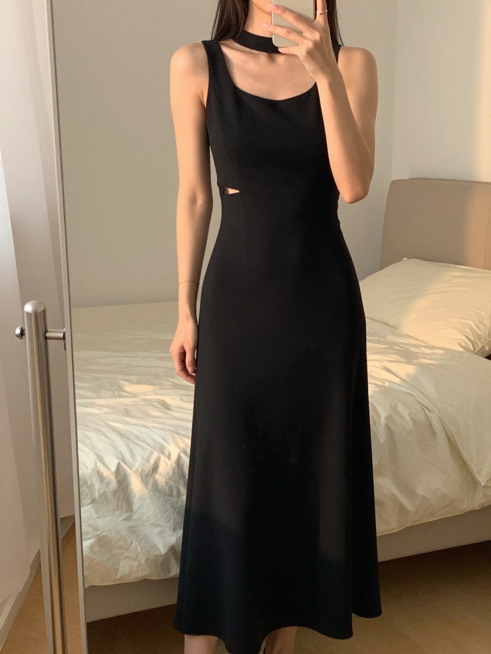 iPhone mirror selfie of a woman in an asymmetrical black maxi, showcasing the unique neckline, cropped at NECK so face doesn't show, in a feminine-themed bedroom, evening golden hour, iPhone photo quality.