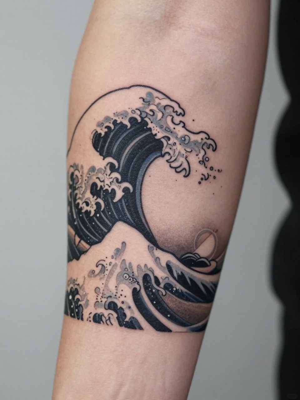 extreme close-up of a clean Japanese wave and sun tattoo on the forearm, curling wave form with simple sun detail, black and grey ink, crisp linework, soft shading, minimalist traditional style, realistic skin texture, soft minimal background, design-focused tattoo inspiration photography (no watermarks on images)