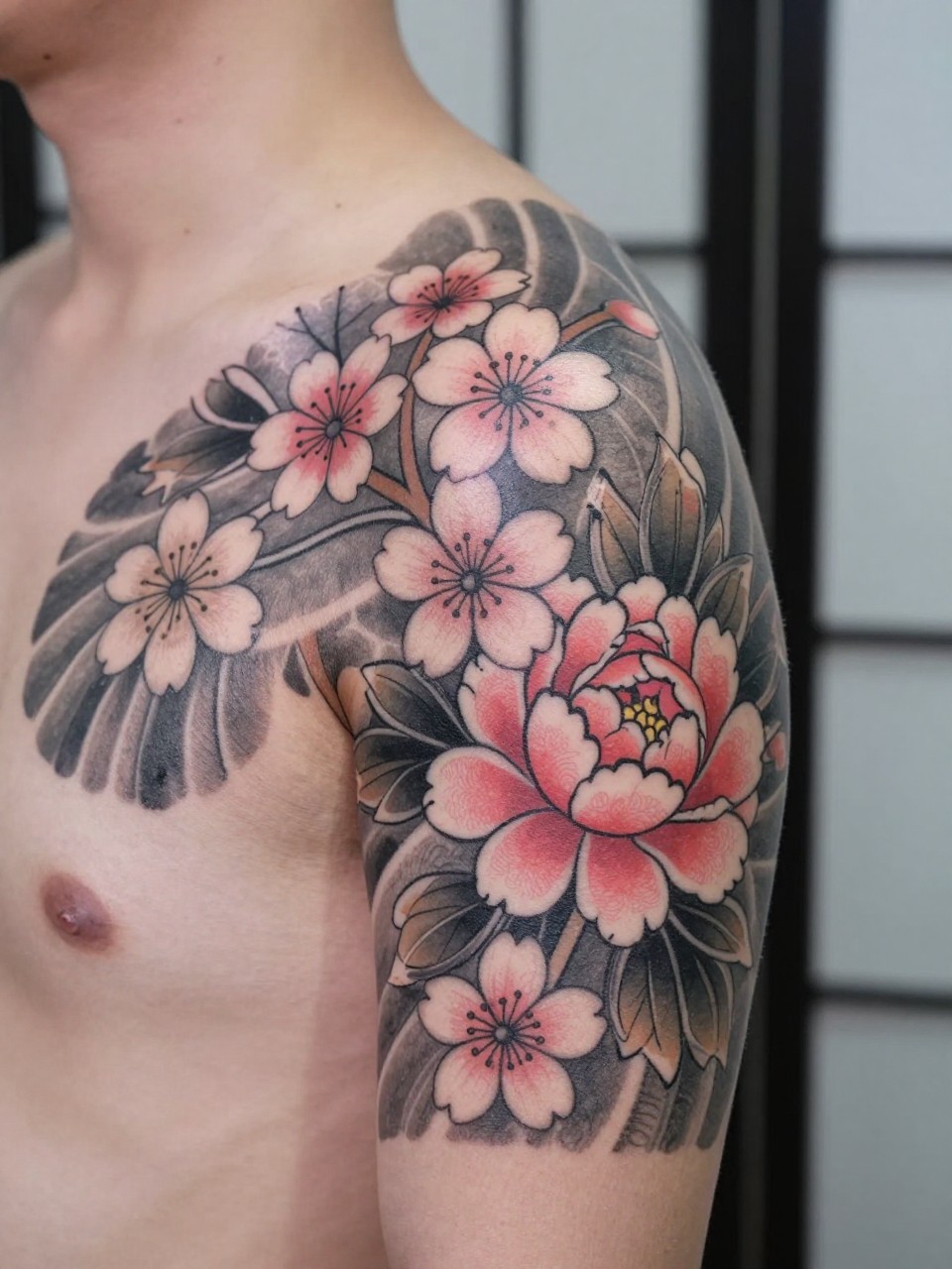 design-focused close-up of a Japanese floral tattoo from shoulder to collarbone, cherry blossoms and peony details flowing with the body, black and grey ink with soft pink and red accents, clean traditional linework, realistic skin texture, minimal blurred background, modern tattoo inspiration photo (no watermarks on images)