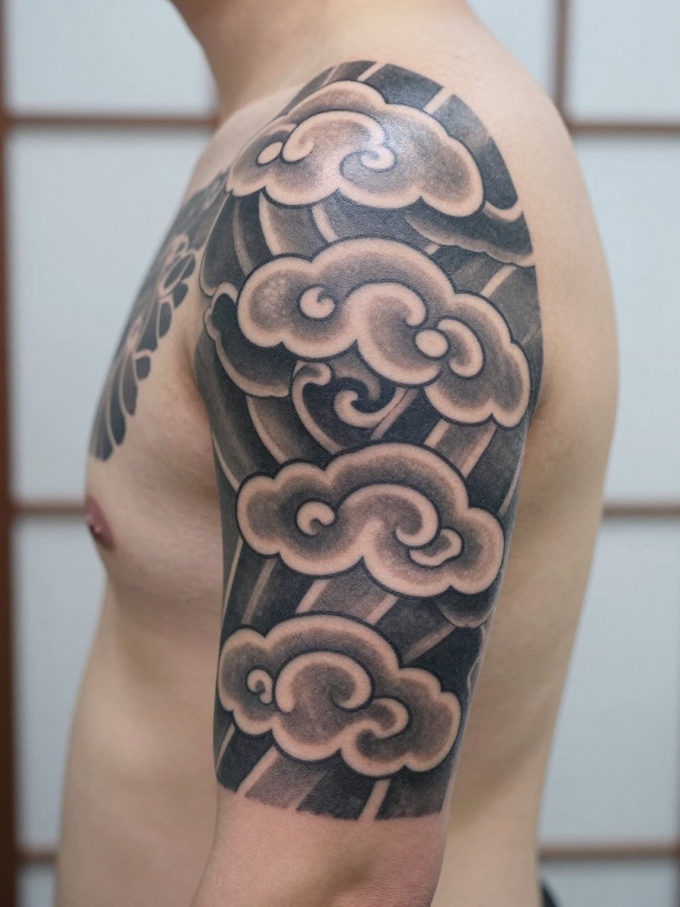 design-focused close-up of a Japanese cloud armband tattoo on the upper arm, repeating traditional cloud shapes wrapping around the arm, black and grey ink, crisp linework, soft shading, realistic skin texture, minimal blurred background, modern tattoo inspiration photo (no watermarks on images)