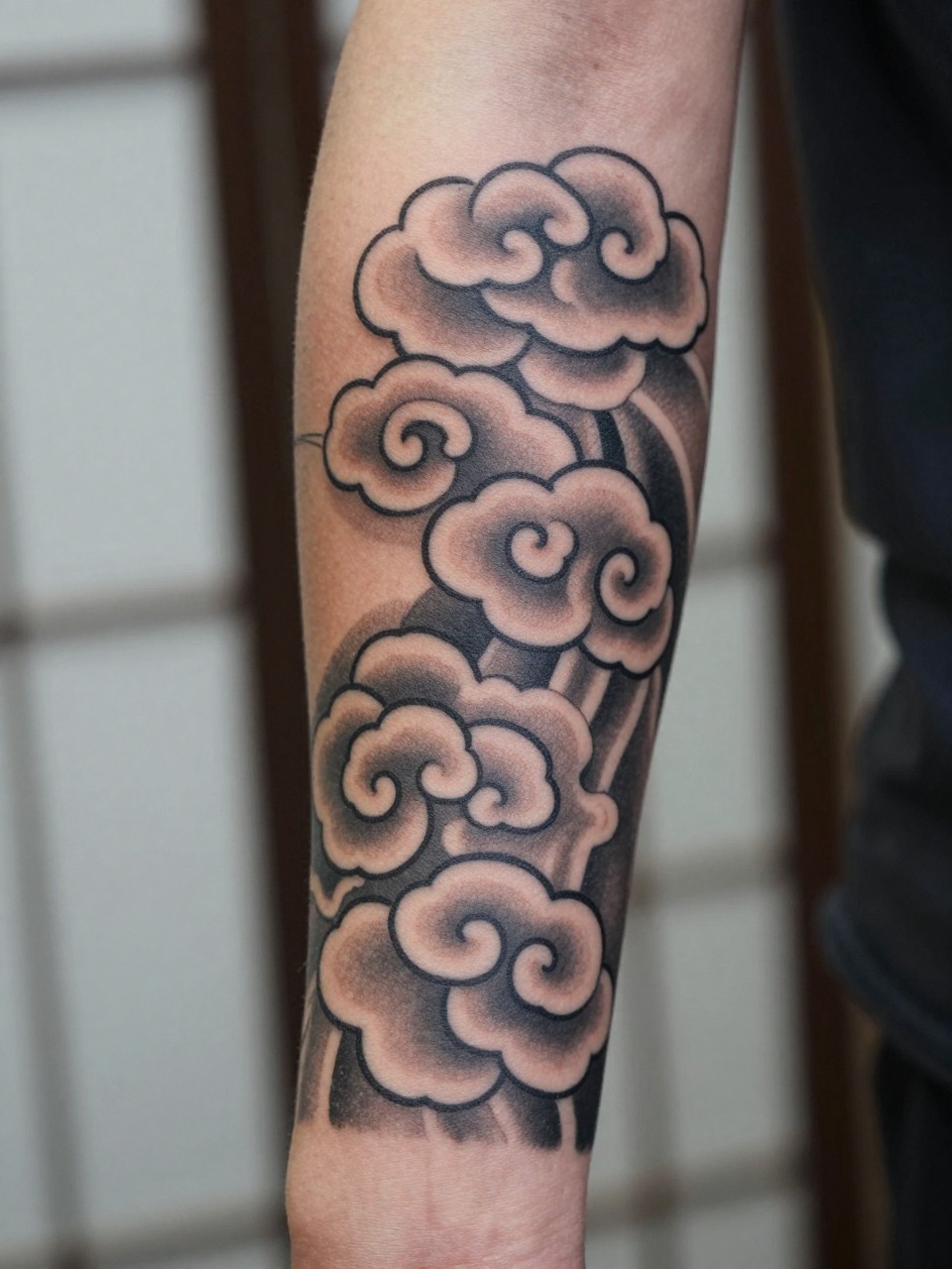 design-focused close-up of a Japanese cloud band tattoo above the elbow, repeating traditional cloud forms wrapping the arm, black and grey ink, clean bold linework, soft shading, realistic skin texture, minimal blurred background, modern tattoo inspiration photo (no watermarks on images)
