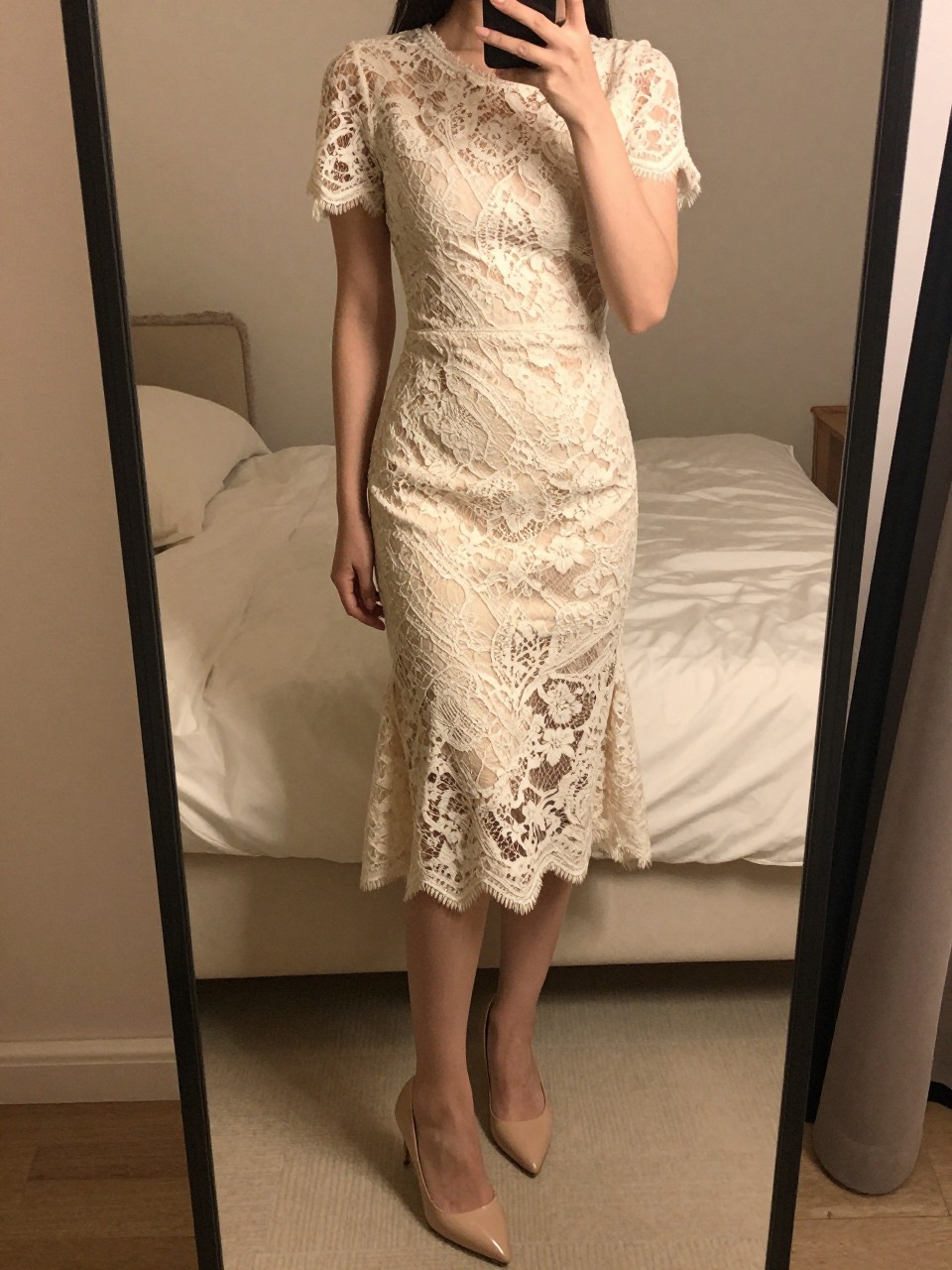 iPhone mirror selfie of a woman in a lace midi dress and nude pumps, gently smoothing the dress, cropped at the neck so face doesn't show, in a feminine-themed bedroom, warm moody lighting, iPhone photo quality.