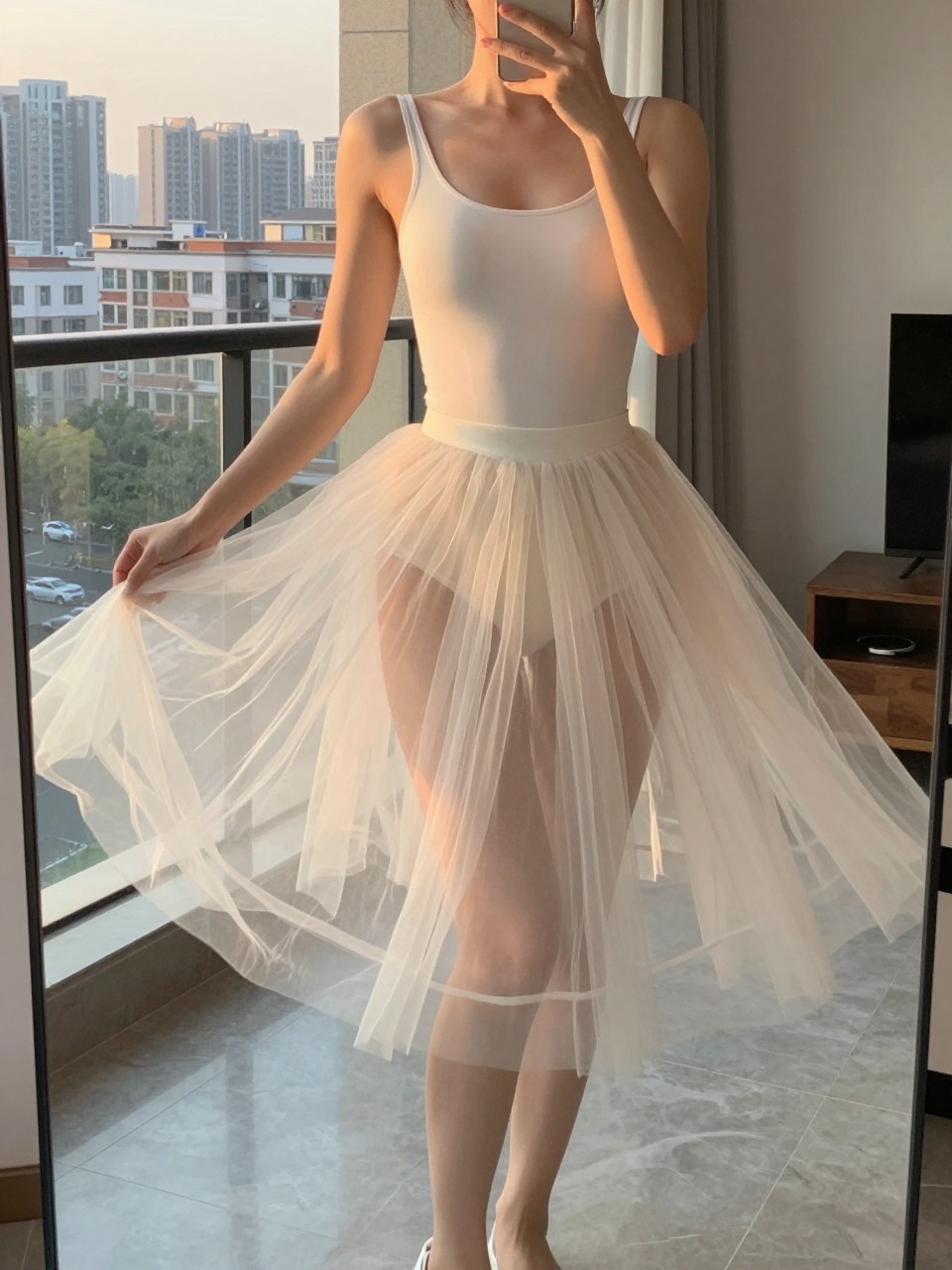 iPhone mirror selfie of a woman in a tulle skirt and bodysuit, twirling to make the skirt float, cropped at the neck so face doesn't show, in a city apartment, evening golden hour lighting, iPhone photo quality.
