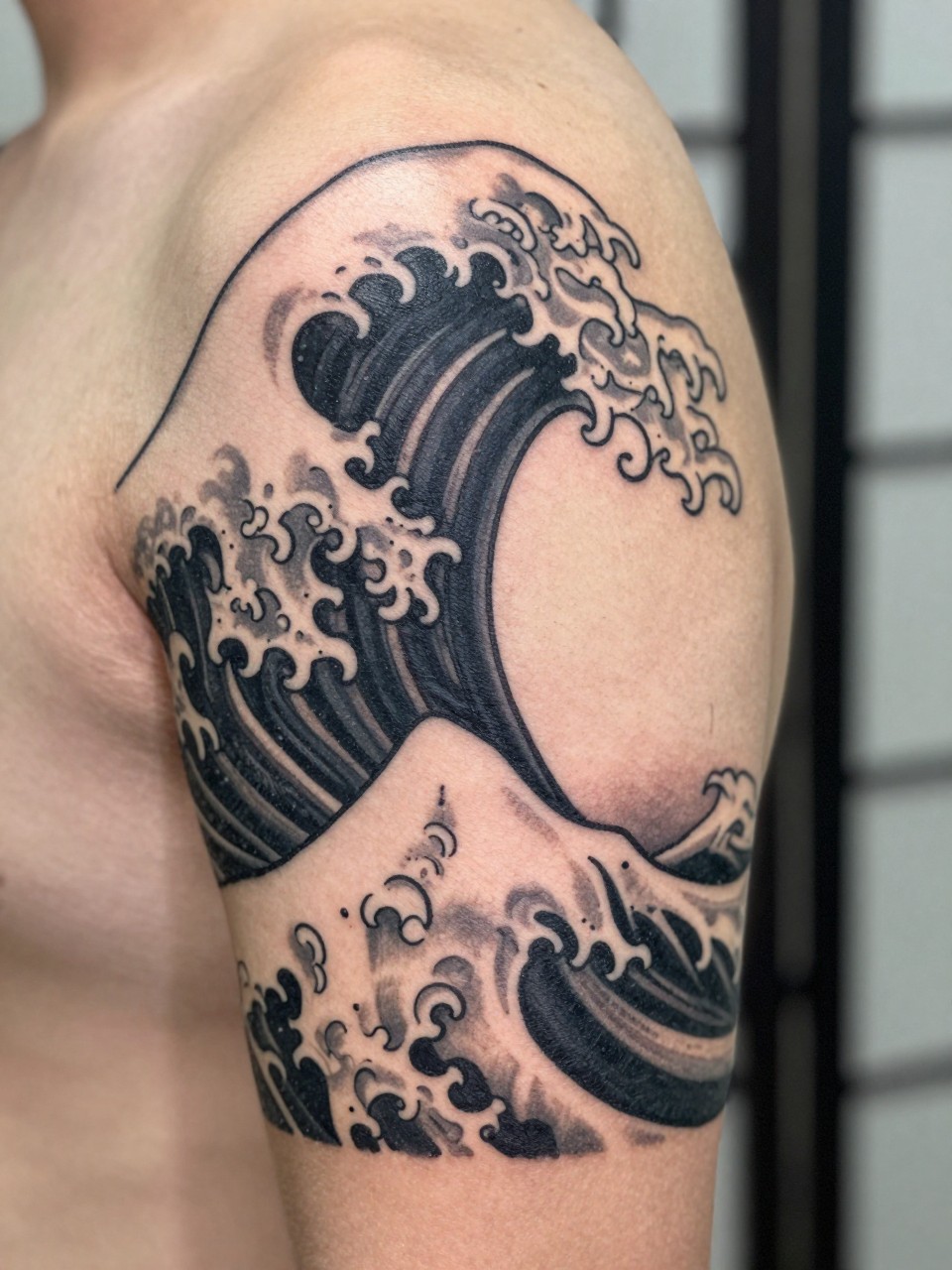 close-up of a clean single Japanese wave tattoo with open negative space on the upper arm, black and grey ink, bold curling wave, crisp traditional linework, soft shading, realistic skin texture, design-focused close-up, blurred neutral background, modern tattoo photography (no watermarks on images)