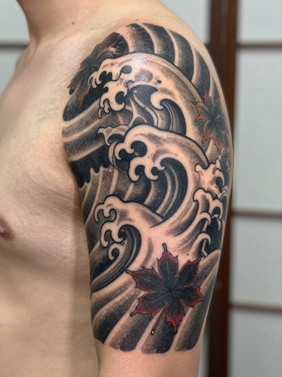 close-up of a traditional Japanese wave and maple leaf tattoo on the arm, curling wave forms, scattered leaves, black and grey ink, bold traditional linework, soft shading, realistic skin texture, design-focused close-up, neutral blurred background, modern tattoo photography (no watermarks on images)