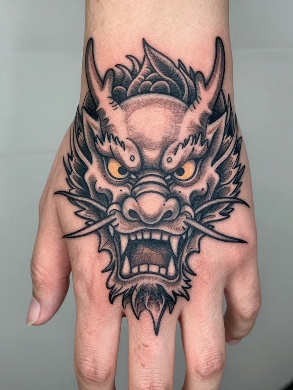 design-focused close-up of a traditional Japanese dragon head tattoo across the back of the hand, detailed scales, flowing whiskers, sharp eyes, black and grey ink, bold linework, soft shading, realistic skin texture, tight crop, minimal blurred background, modern tattoo inspiration photo (no watermarks on images)