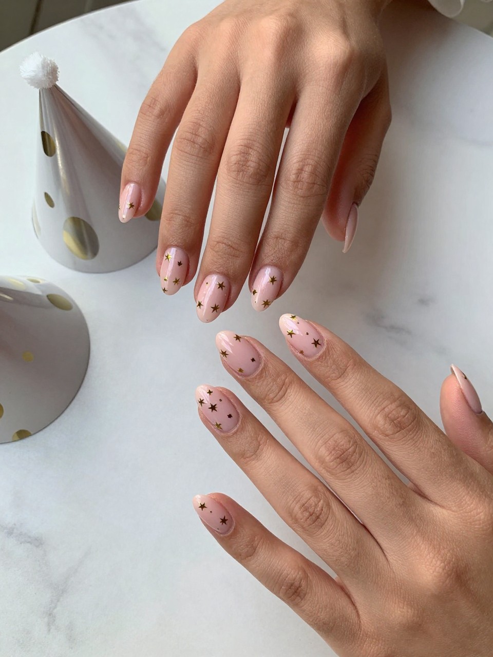 90-degree overhead top-down view of two feminine black hands with almond medium nails.
The manicure features a blush pink base with tiny metallic gold star accents scattered across two nails.
Include glossy gel finish.

Hands are posed fingers gently spread.

Scene set on a marble surface with a small party hat nearby.

Bright natural daylight with soft shadows, hyper-realistic lifestyle photography, sharp focus on nails, natural skin texture, realistic hands, no extra fingers.