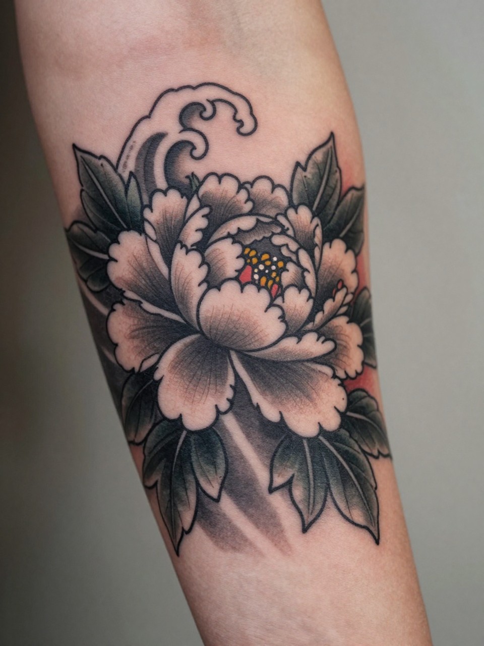 macro shot of a Japanese peony and wave tattoo on the forearm, blooming peony with curling wave details, black and grey ink, subtle red petal accents, bold traditional linework, realistic skin texture, design-first tattoo image, soft neutral background, tattoo inspiration image (no watermarks on images)