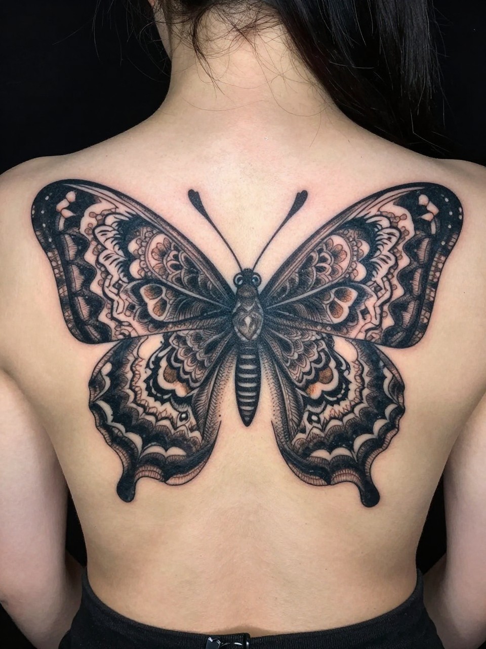"Direct back-of-neck view: a wide, intricate owl butterfly tattoo with mandala-patterned wings spanning the entire nape. Sharp, symmetrical, and covering the area with detailed boldness."
