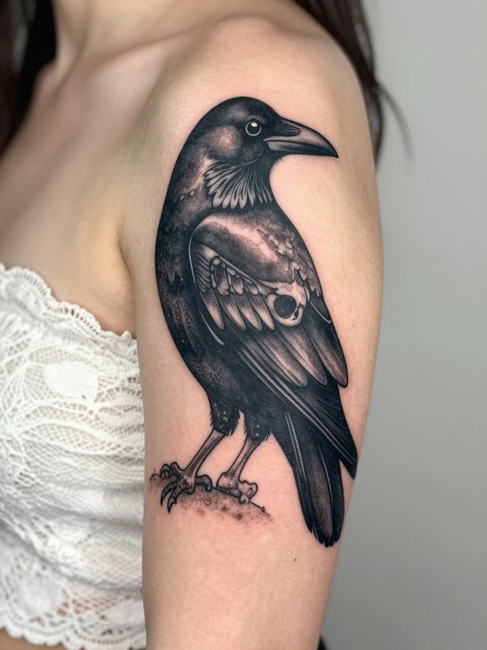  "tight crop of a black crow and skull tattoo on the upper arm, dark black ink, soft grey shading, detailed feathers and bone texture, bold clean linework, realistic skin texture, lace fabric detail nearby, minimal soft background, dramatic tattoo inspiration image (no watermarks on images)"